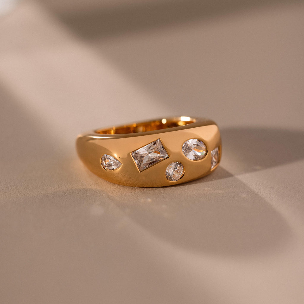 The Diamond Confetti Signet Ring, featuring four sparkling diamonds, sits elegantly on a smooth beige surface under soft lighting.