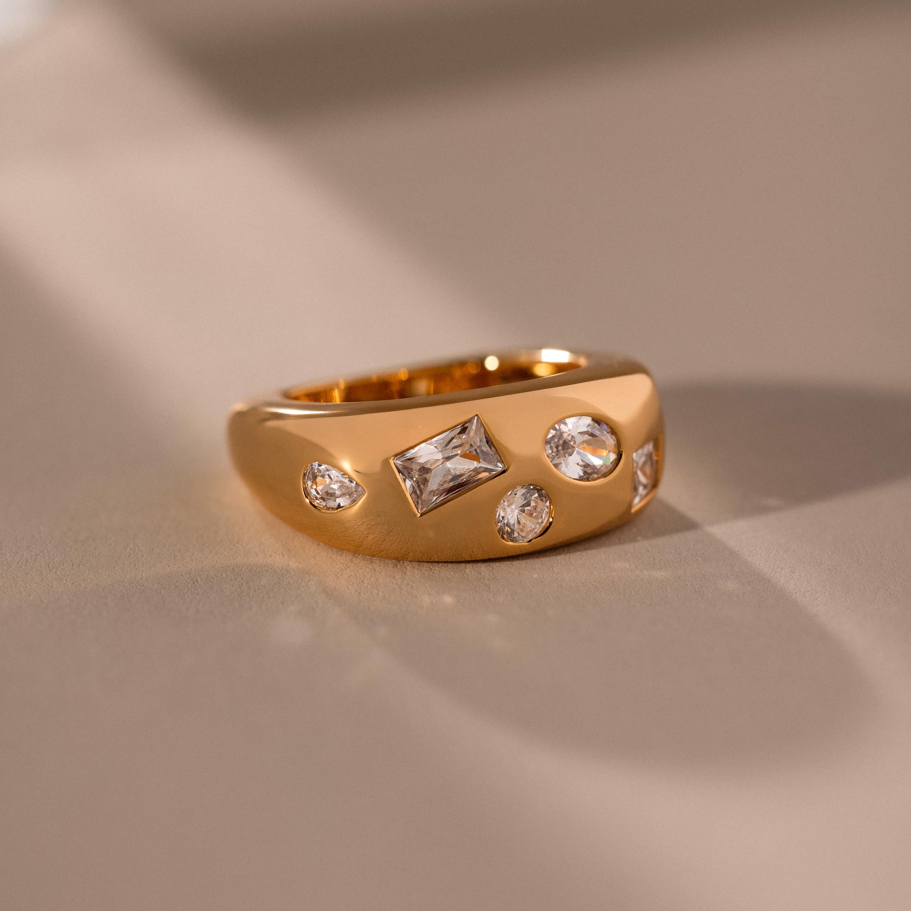 The Diamond Confetti Signet Ring, featuring four sparkling diamonds, sits elegantly on a smooth beige surface under soft lighting.