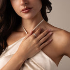 A woman in a cream dress touches her chest, highlighting the Skinny Pave Stacking Ring on her finger against a neutral background.