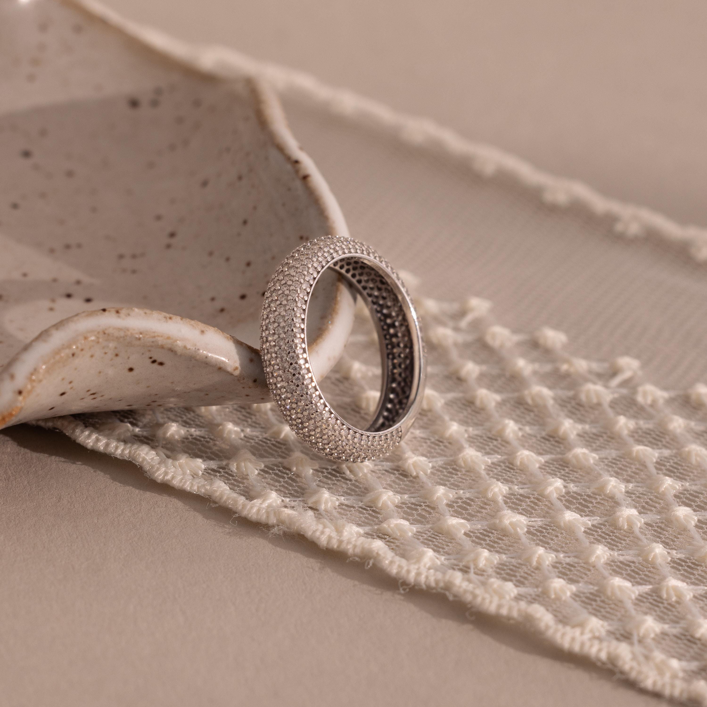 The Bold Pave Stacking Ring with a textured silver dome design rests on a ceramic dish atop woven cream-colored fabric.