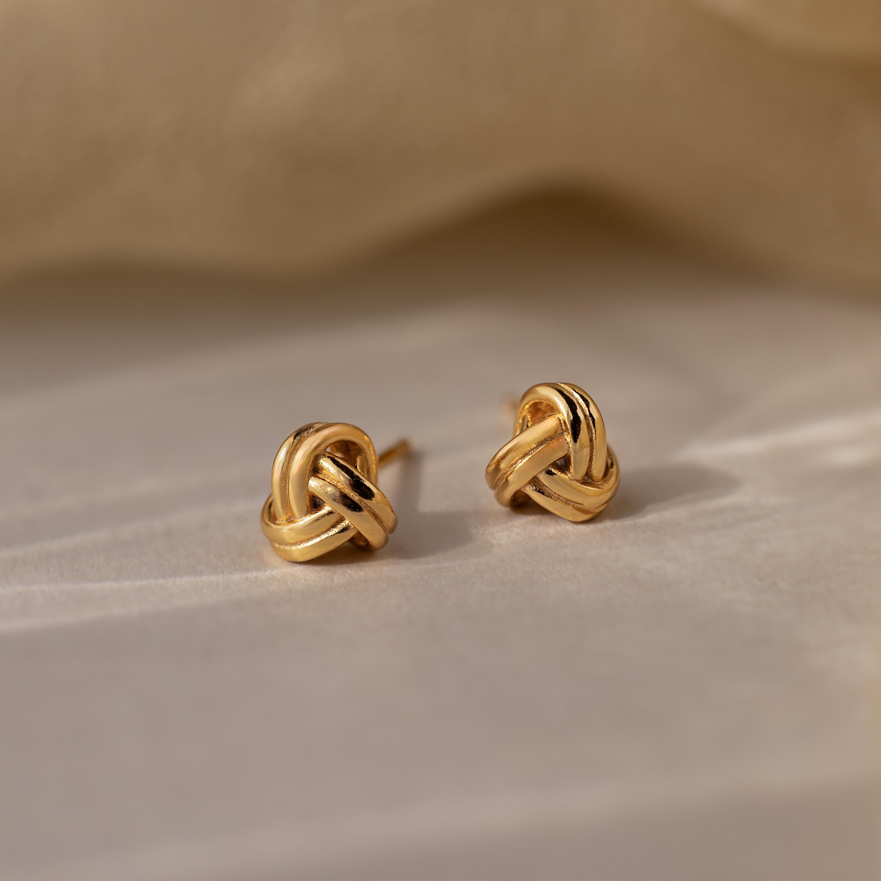 Pair of gold knot earrings on a beige fabric background