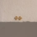 Rounded Pearl Flower Studs featuring a gold bezel, floral design, and white pearls—an elegant choice for bridesmaid jewelry—displayed on a textured off-white surface.