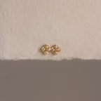 Rounded Pearl Flower Studs featuring a gold bezel, floral design, and white pearls—an elegant choice for bridesmaid jewelry—displayed on a textured off-white surface.
