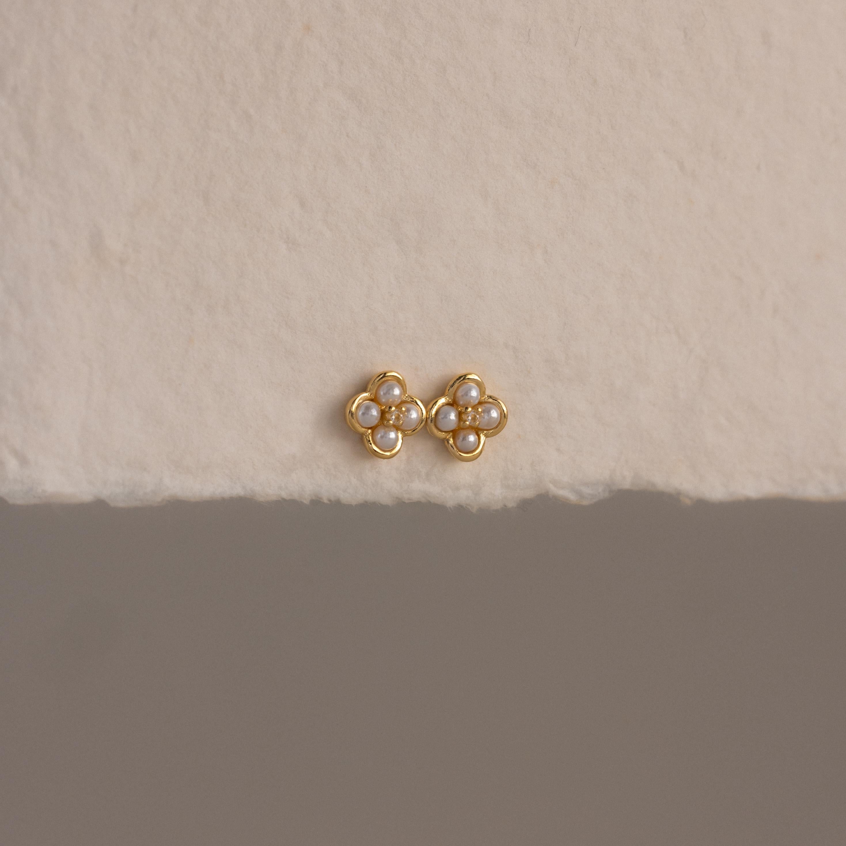 Rounded Pearl Flower Studs featuring a gold bezel, floral design, and white pearls—an elegant choice for bridesmaid jewelry—displayed on a textured off-white surface.