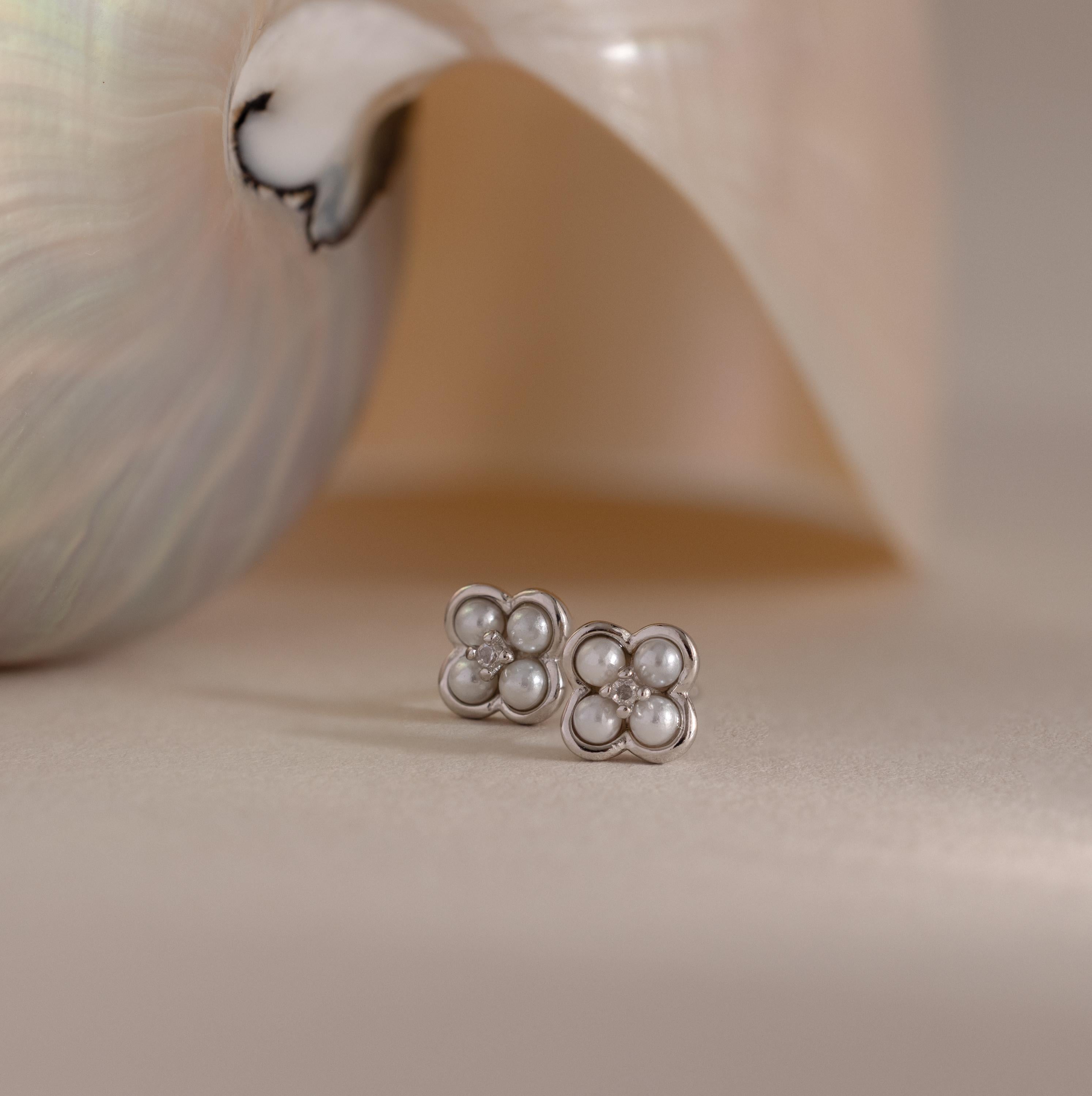 Rounded Pearl Flower Studs in Sterling Silver, featuring pearl centers and floral designs, are displayed before a shiny seashell on a beige surface—an elegant option for bridesmaid jewelry.