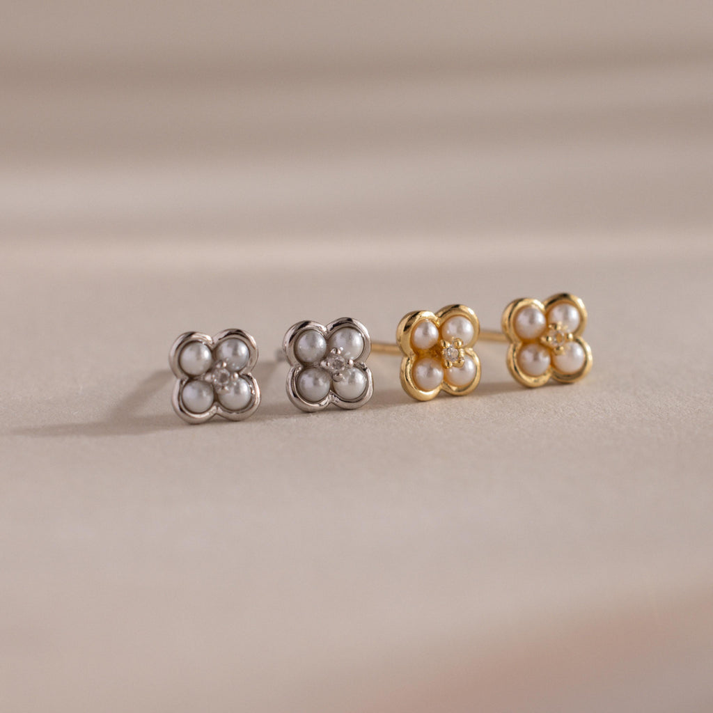 The Rounded Pearl Flower Studs, featuring pearl and crystal accents in gold and silver floral shapes, make an elegant bridesmaid jewelry choice, beautifully displayed on a beige surface.