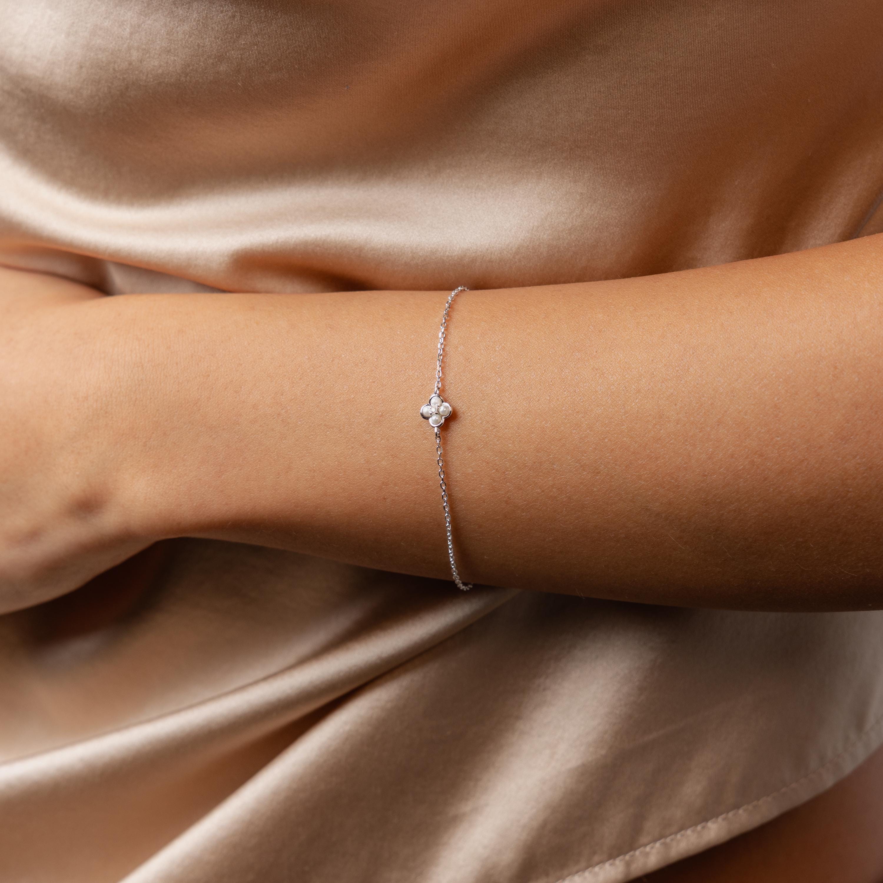 The Rounded Pearl Flower Bracelet in Sterling Silver, featuring a delicate floral charm, rests gracefully on a woman’s wrist against a satin dress.
