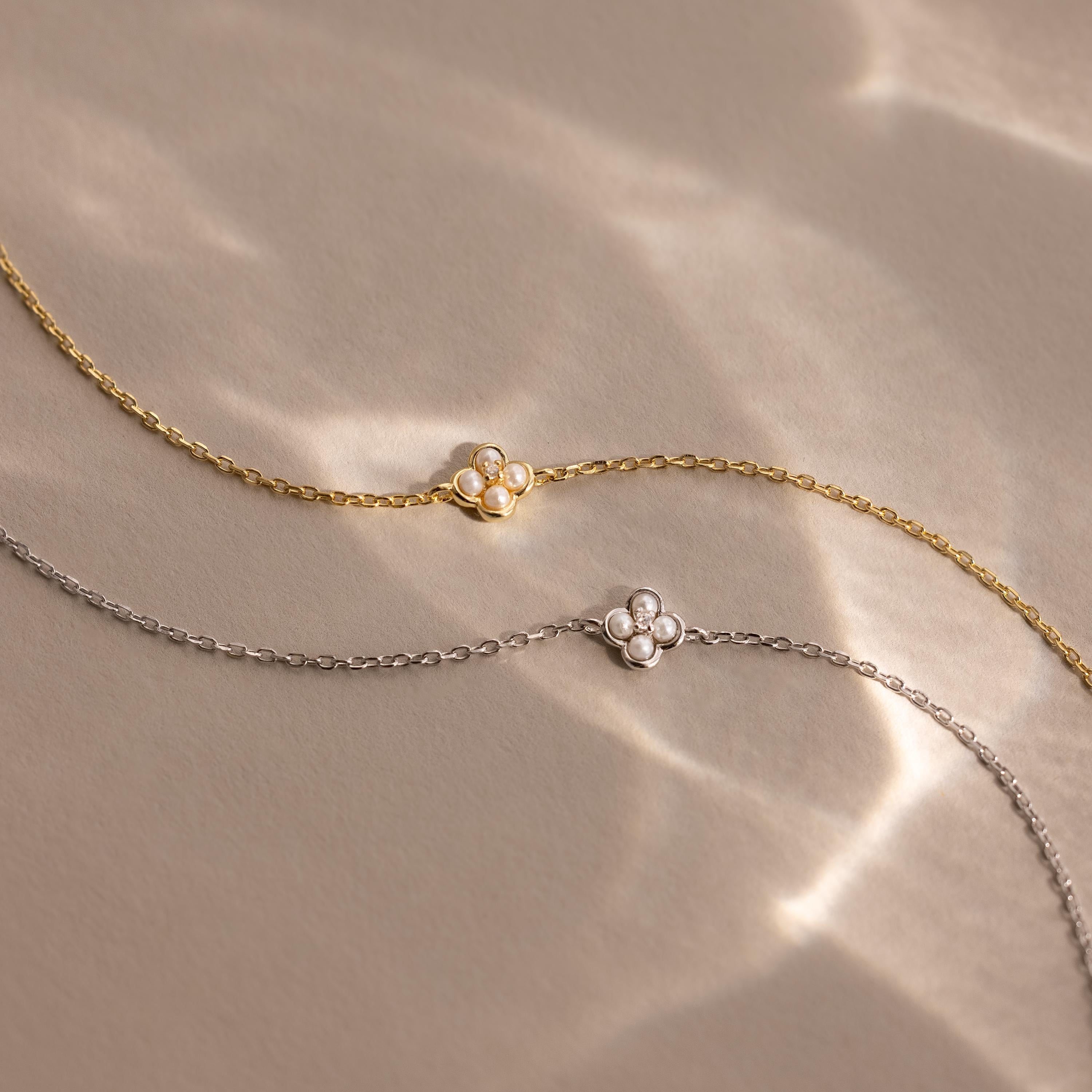 The Rounded Pearl Flower Bracelet comes in gold or silver, each with a delicate chain and a pearl flower charm—ideal for layering or wearing solo as timeless jewelry. Shown on a neutral background.