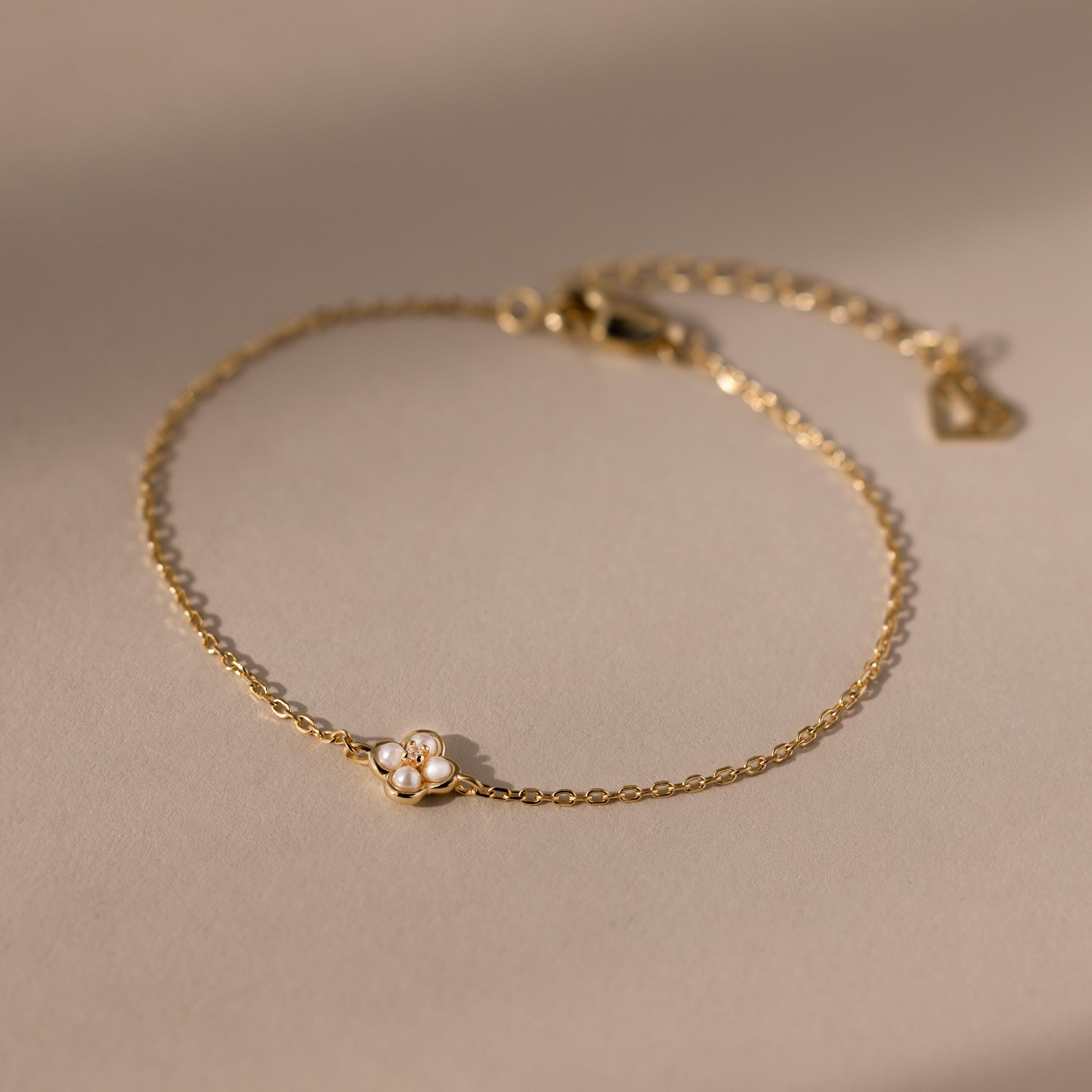 The Rounded Pearl Flower Bracelet features a delicate gold chain with a petite pearl flower charm, making it an elegant choice for everyday wear and perfect for fans of subtle, refined jewelry.