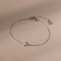 The Rounded Pearl Flower Bracelet in Sterling Silver features a small floral charm and three tiny pearls, beautifully displayed on a beige background.
