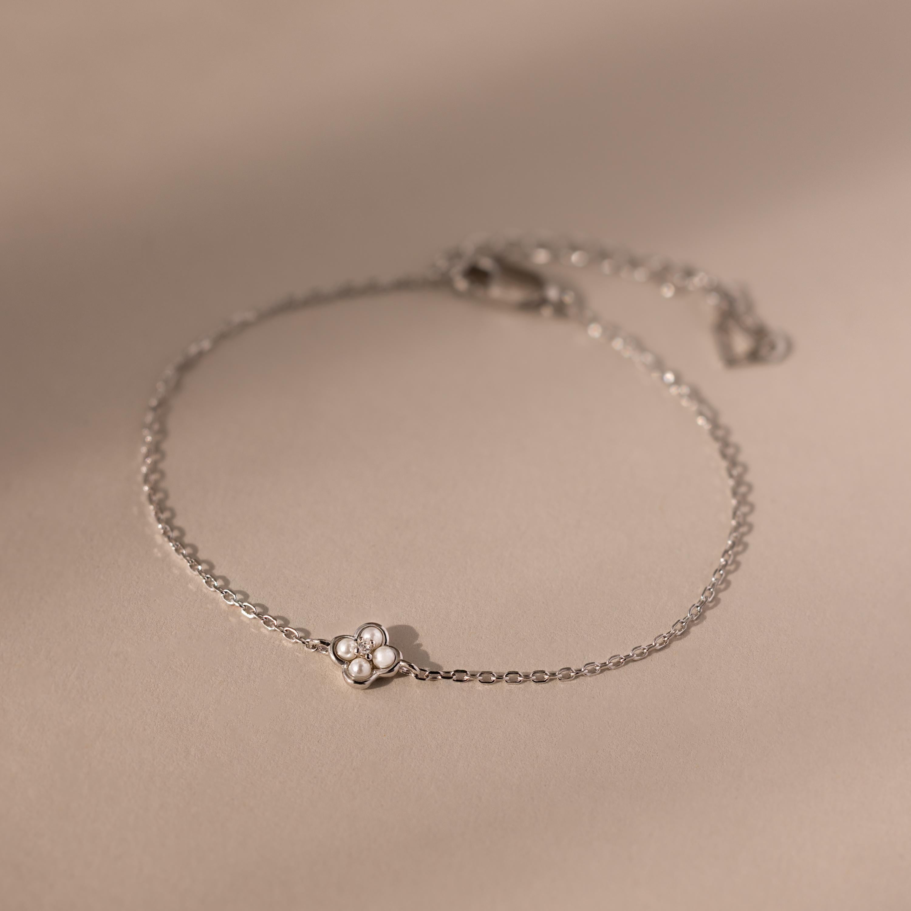 The Rounded Pearl Flower Bracelet in Sterling Silver features a small floral charm and three tiny pearls, beautifully displayed on a beige background.