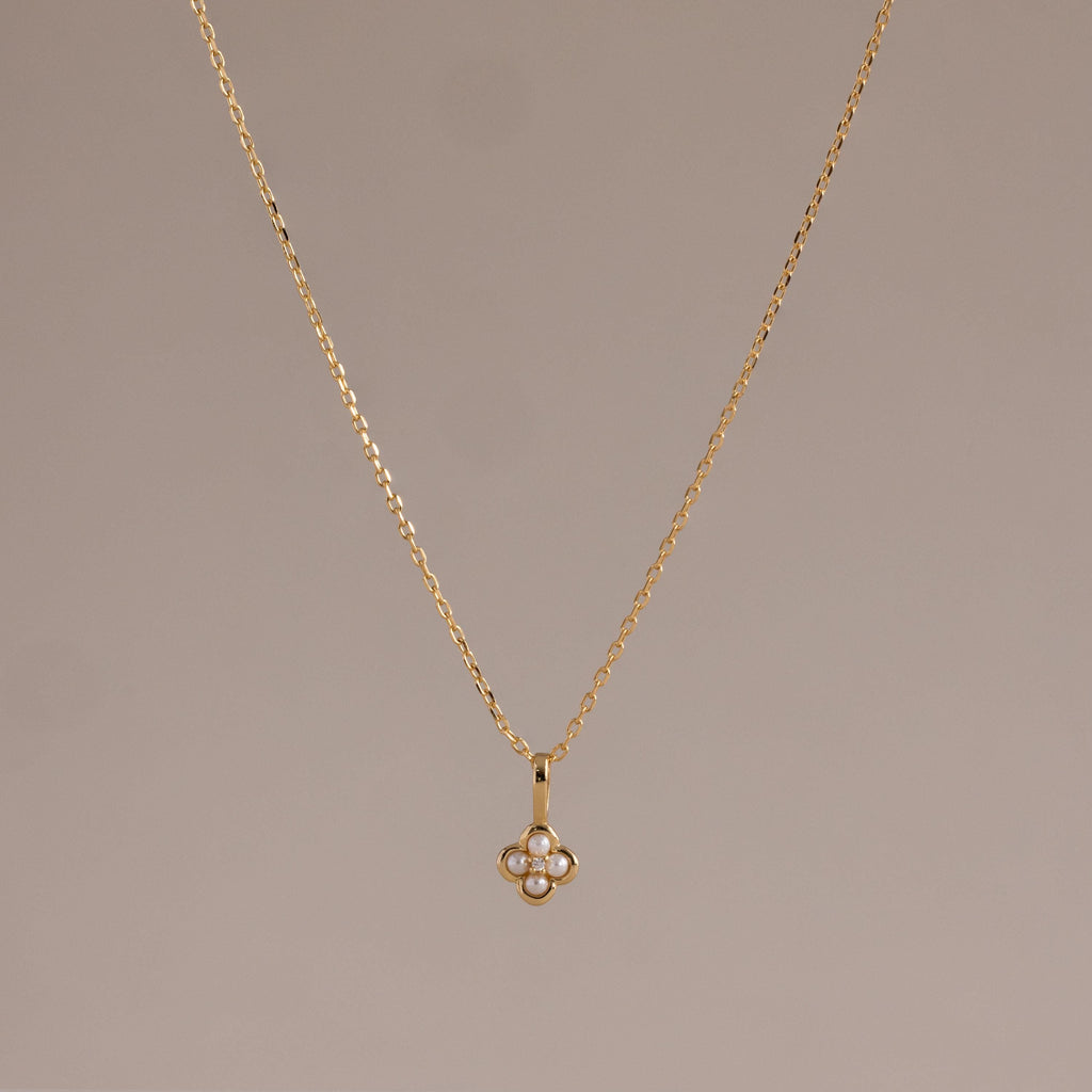 The Rounded Pearl Flower Necklace in 18K Gold features a delicate, four-petal floral pendant accented with white stones—ideal for lovers of subtle, feminine jewelry. Shown on a neutral background.