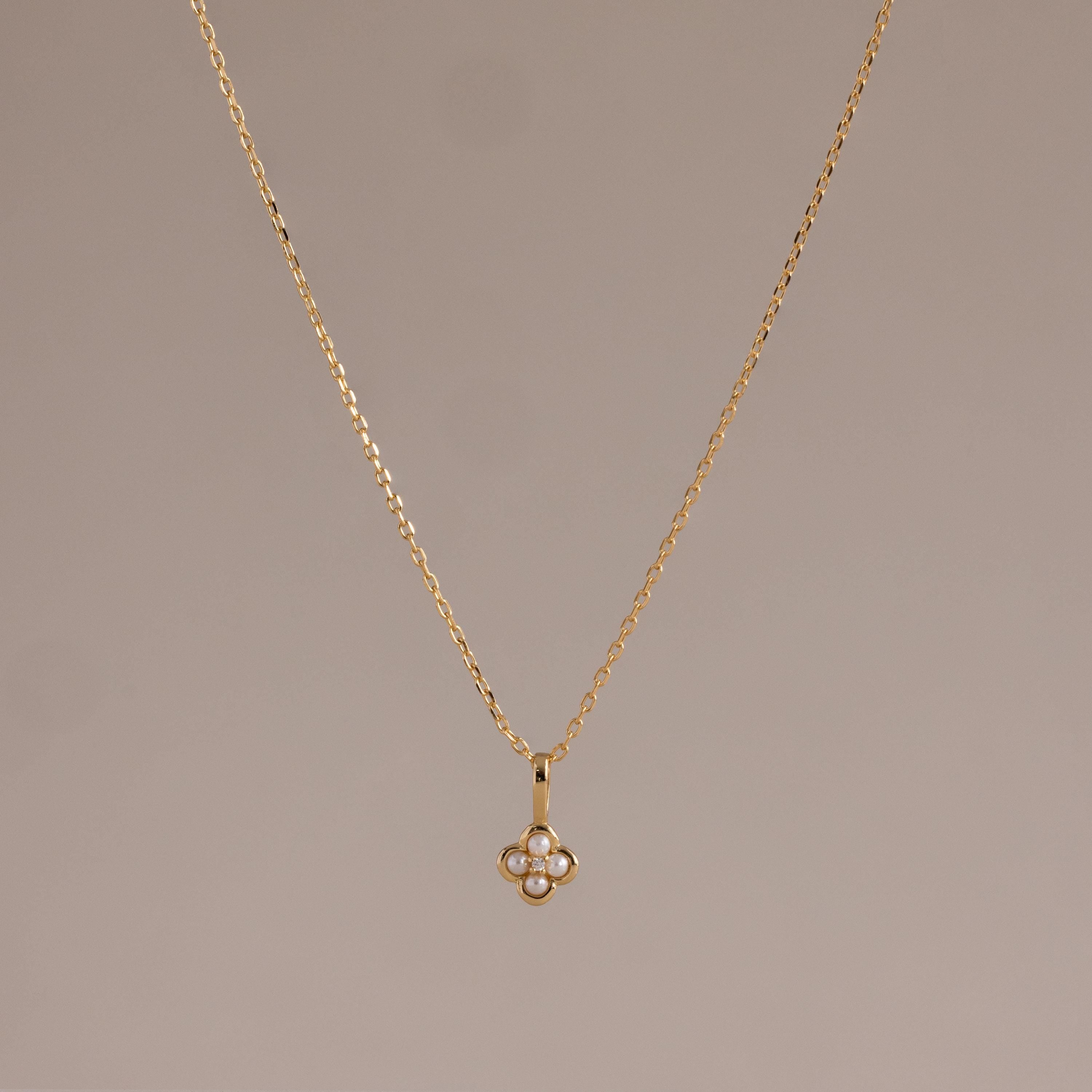 The Rounded Pearl Flower Necklace in 18K Gold features a delicate, four-petal floral pendant accented with white stones—ideal for lovers of subtle, feminine jewelry. Shown on a neutral background.