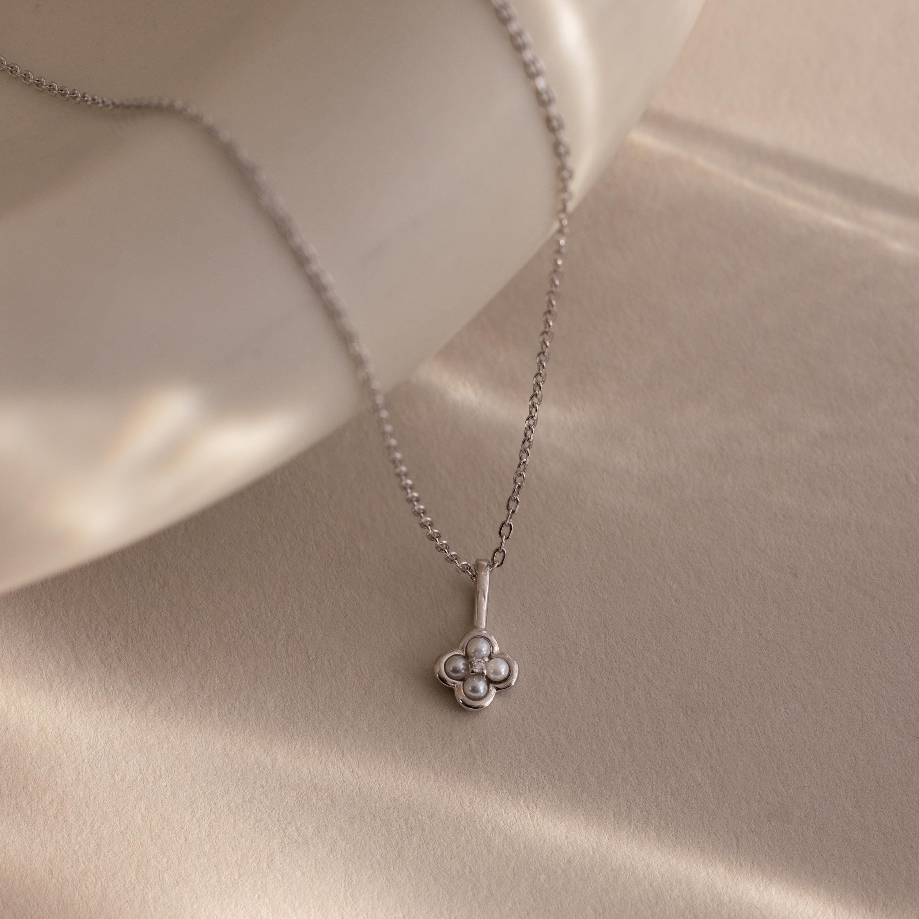 The Rounded Pearl Flower Necklace, featuring a delicate floral pendant, rests on a smooth, light beige surface under soft lighting.