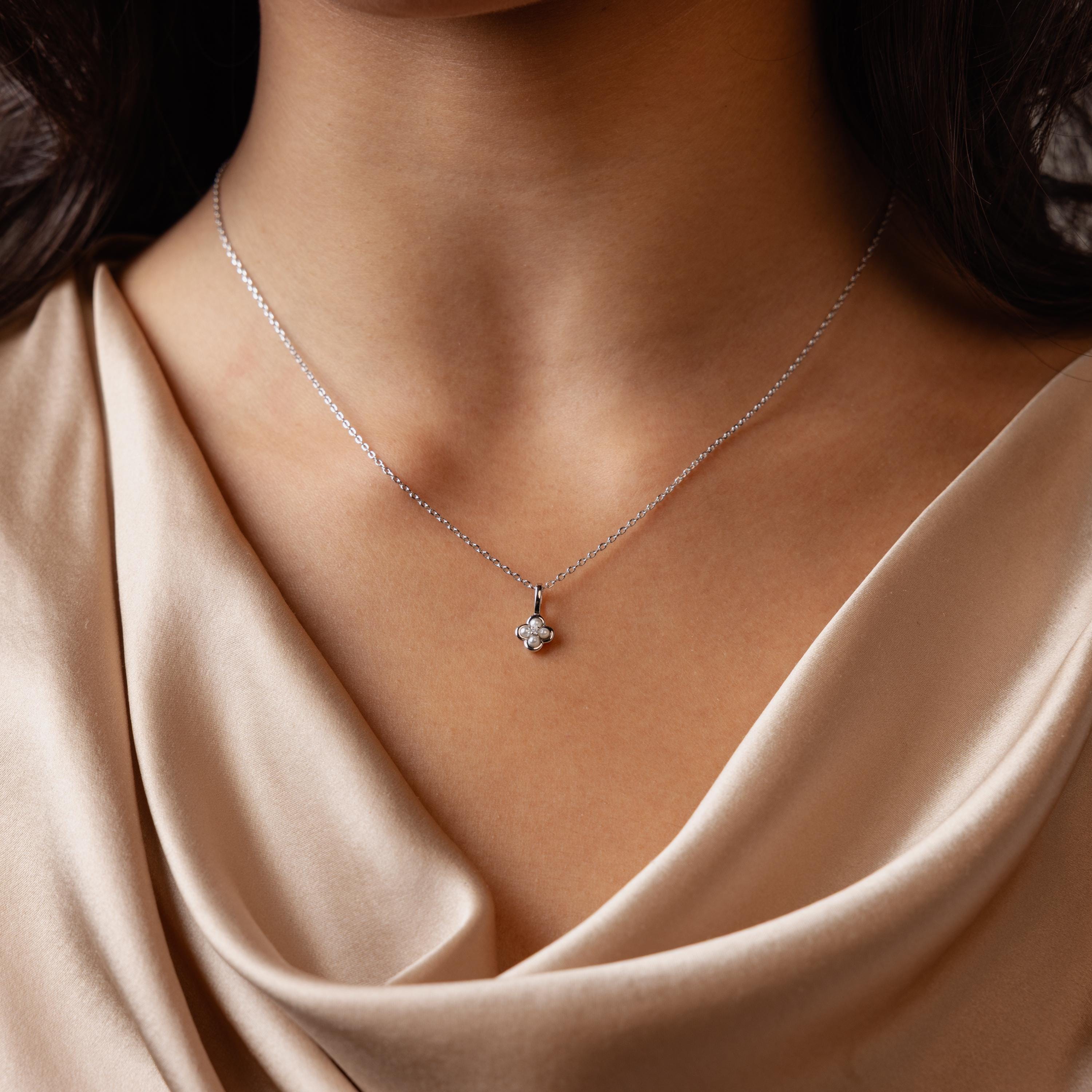 A woman wears the Rounded Pearl Flower Necklace in Sterling Silver, featuring a delicate floral pendant on a silver chain, paired with a beige satin top—perfect for everyday layering.