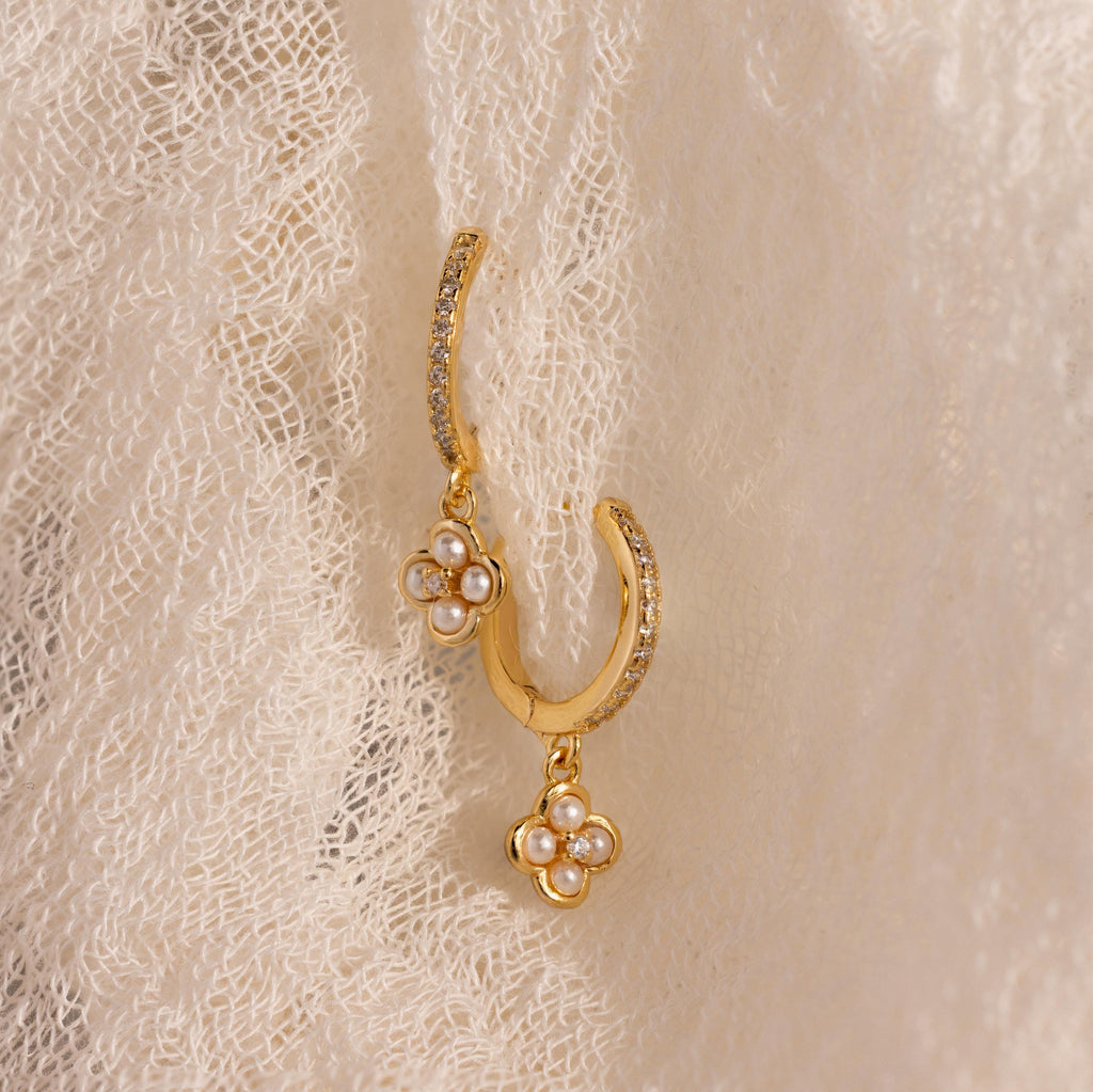 Pave Rounded Pearl Flower Hoops in 18K Gold, shown on textured cream fabric, feature delicate pearl flower charms—ideal for weddings or adding elegance to classic hoop earrings.