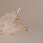 The Pave Rounded Pearl Flower Hoops in 18K Gold feature pearl flower charms and crystal accents, displayed on clear quartz crystals—perfect as elegant wedding earrings.