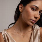 Woman wearing Pave Rounded Pearl Flower Hoops and a matching gold necklace with a small pendant, in a beige satin top.