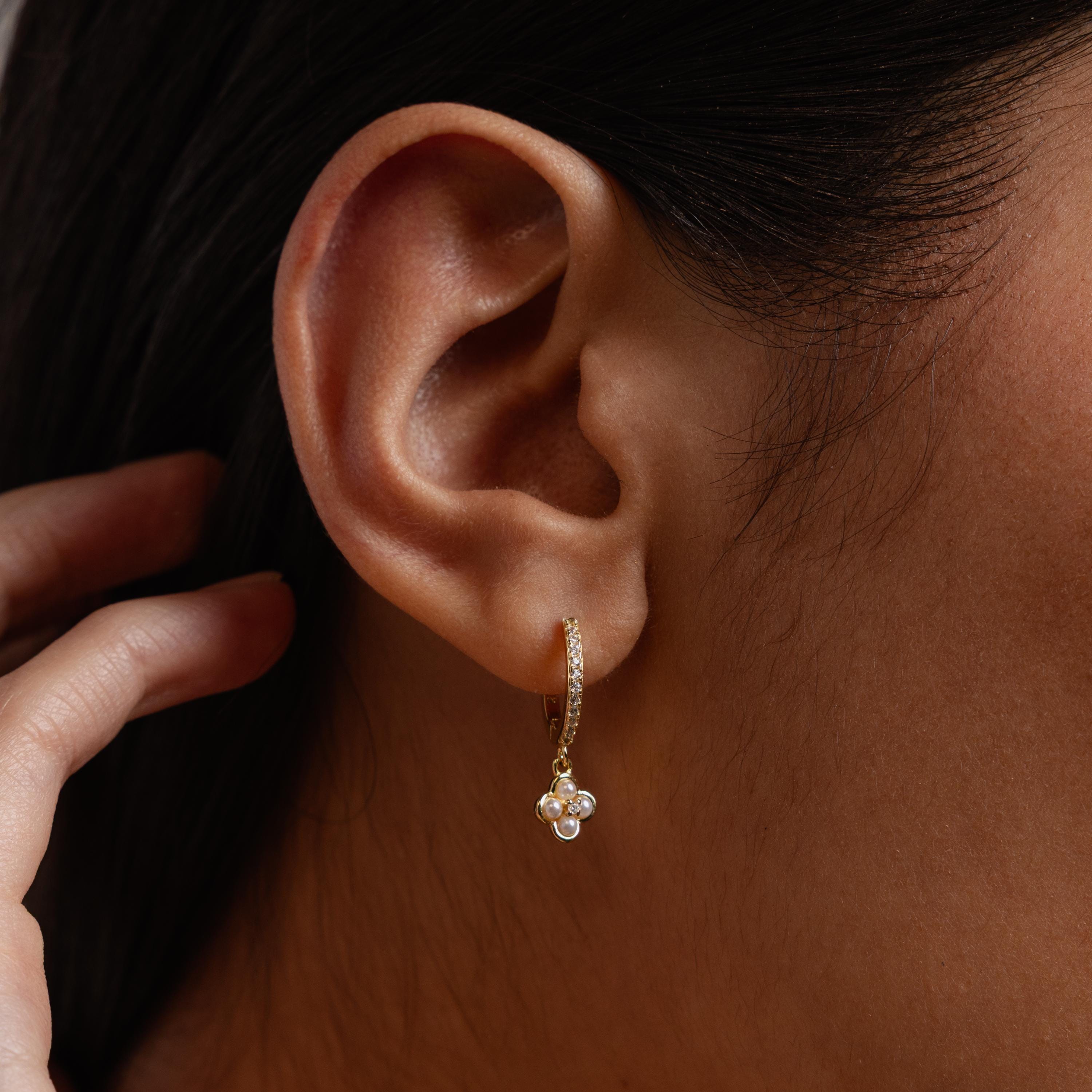Close-up of an ear wearing Pave Rounded Pearl Flower Hoops, elegant gold earrings with small dangling pearls and a hand near the face.