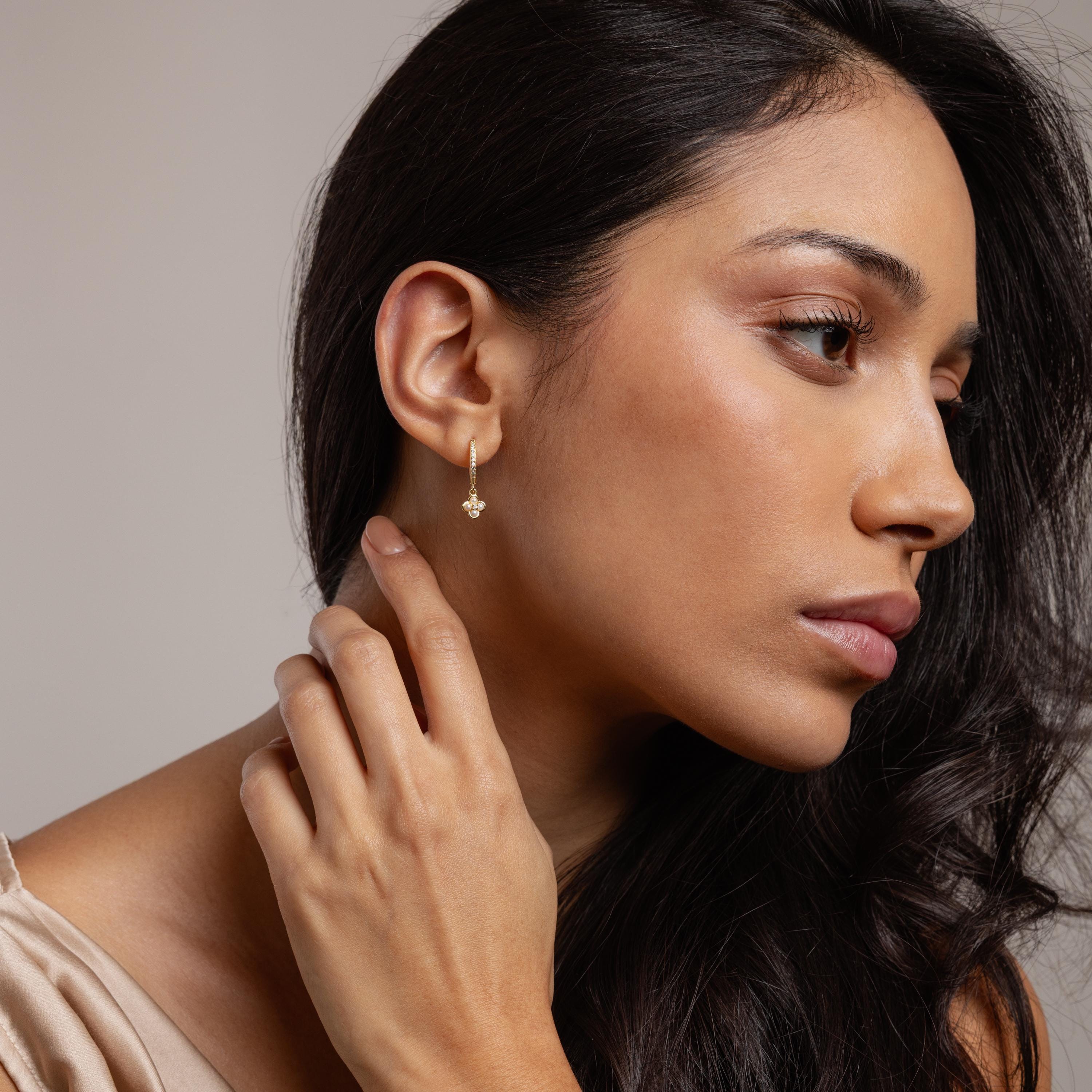 Woman with long dark hair wearing Pave Rounded Pearl Flower Hoops in 18K Gold, touching her neck and gazing to the side.