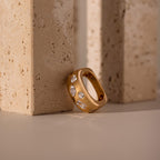 Diamond Confetti Signet Ring with sparkling gemstones rests against beige stone blocks—a modern band that showcases effortless elegance.