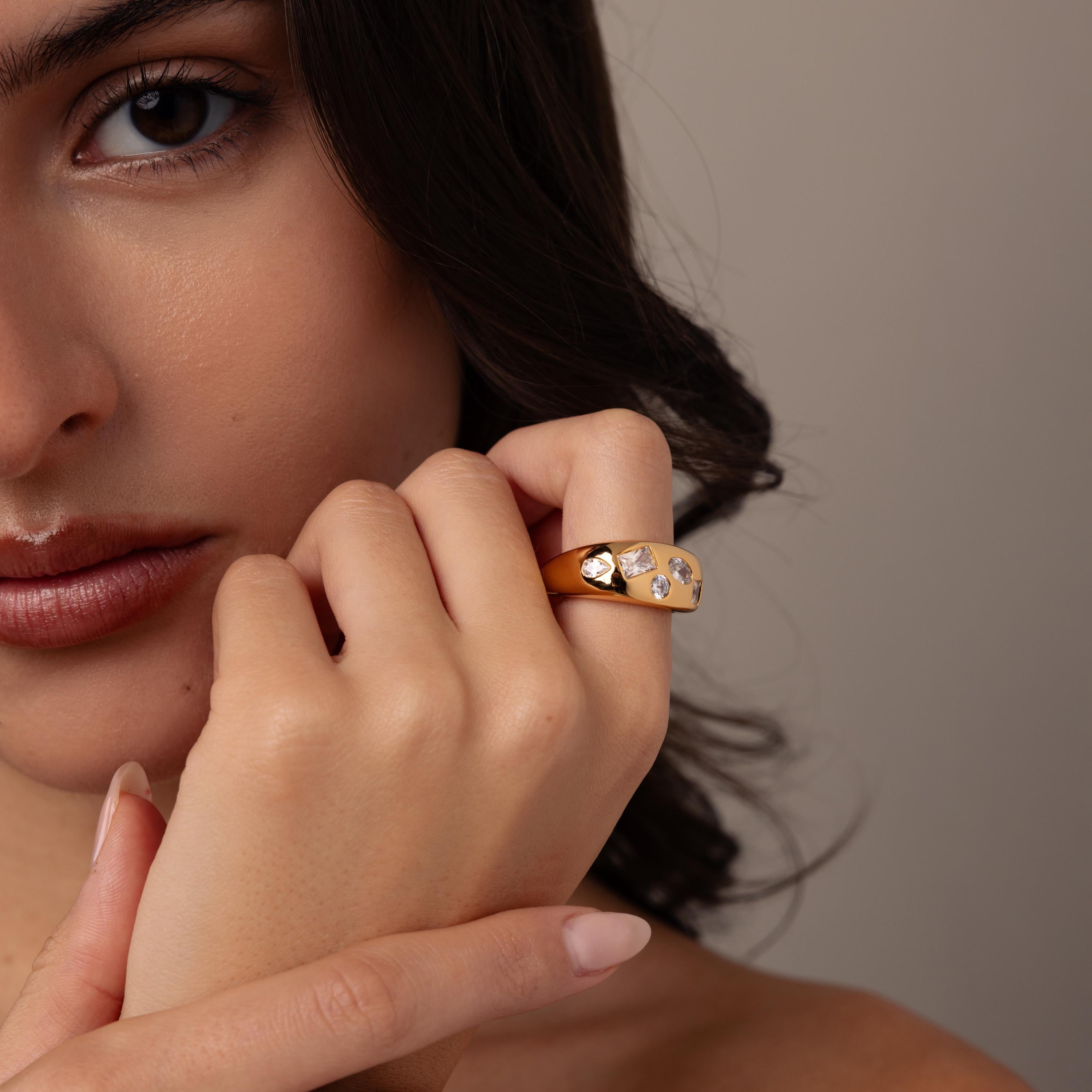 A woman wearing nude lipstick and a modern band, the Diamond Confetti Signet Ring, adorned with sparkling gemstones, gently touches her face.