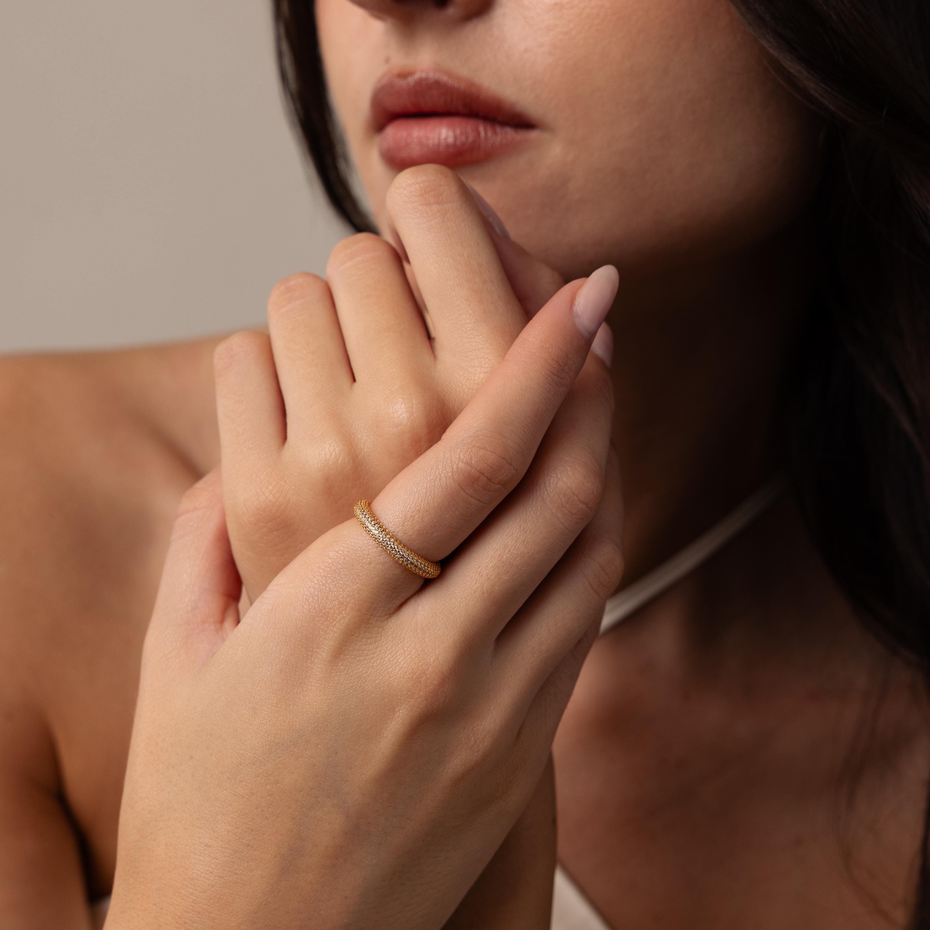 A woman with long brown hair touches her chin while wearing the Skinny Pave Stacking Ring adorned with small pave stones on her finger.