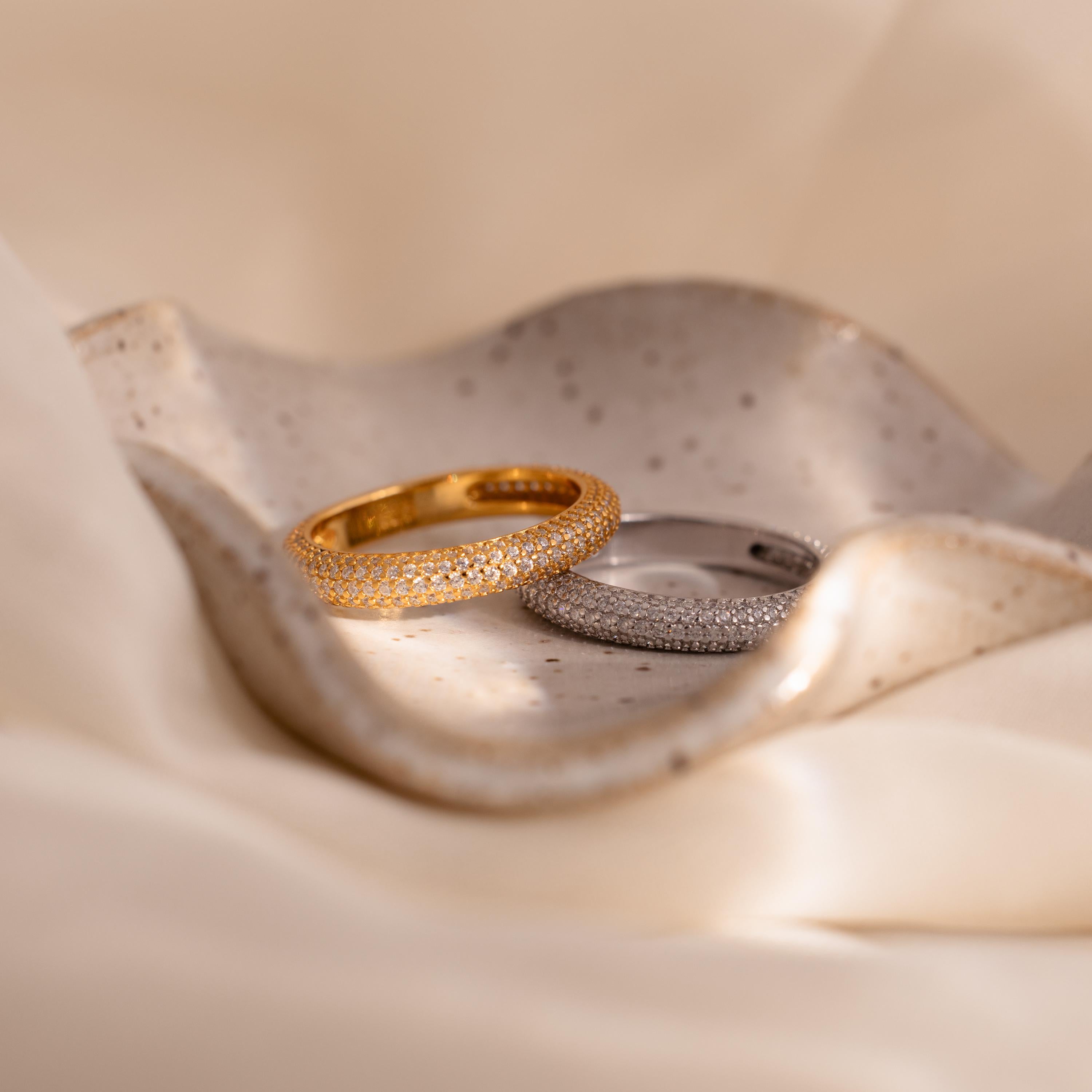A Skinny Pave Stacking Ring sparkles on a textured ceramic dish, with shimmering pave stones and a soft cream fabric backdrop.