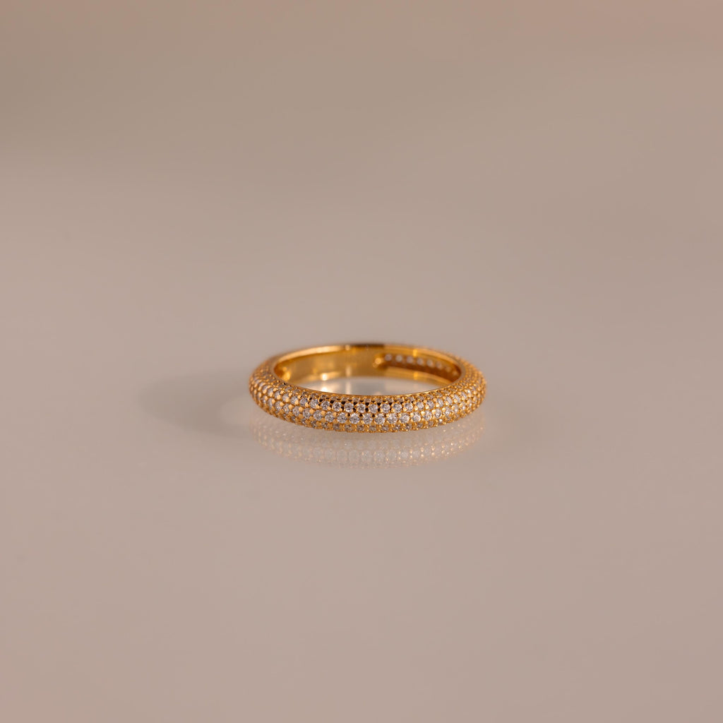 The Skinny Pave Stacking Ring, featuring three rows of sparkling pave stones, rests elegantly on a light-reflective surface.