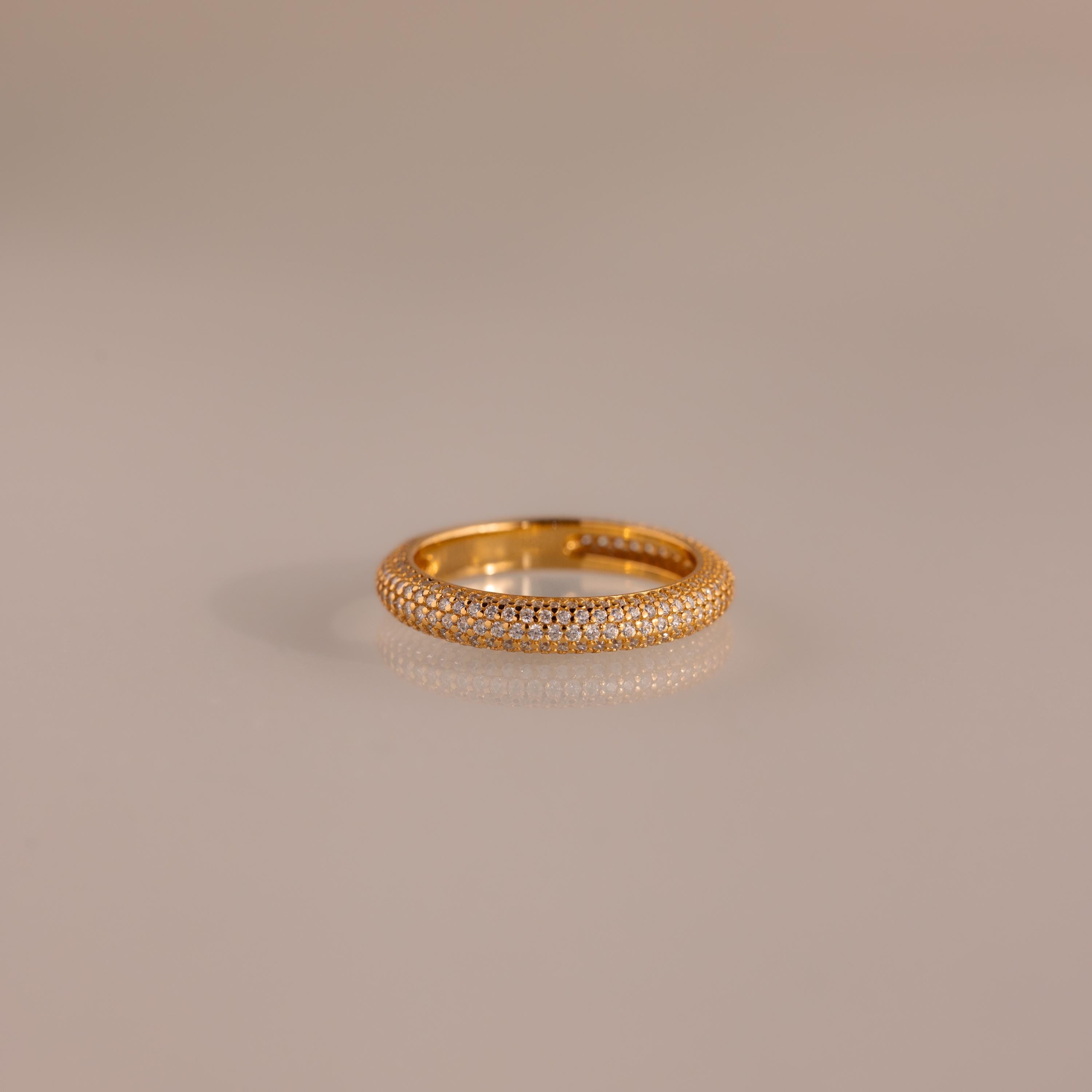 The Skinny Pave Stacking Ring, featuring three rows of sparkling pave stones, rests elegantly on a light-reflective surface.