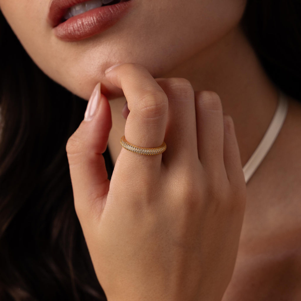 A woman wears the Skinny Pave Stacking Ring, sparkling with pave stones, on her finger as she raises her hand near her face, lips softly parted.