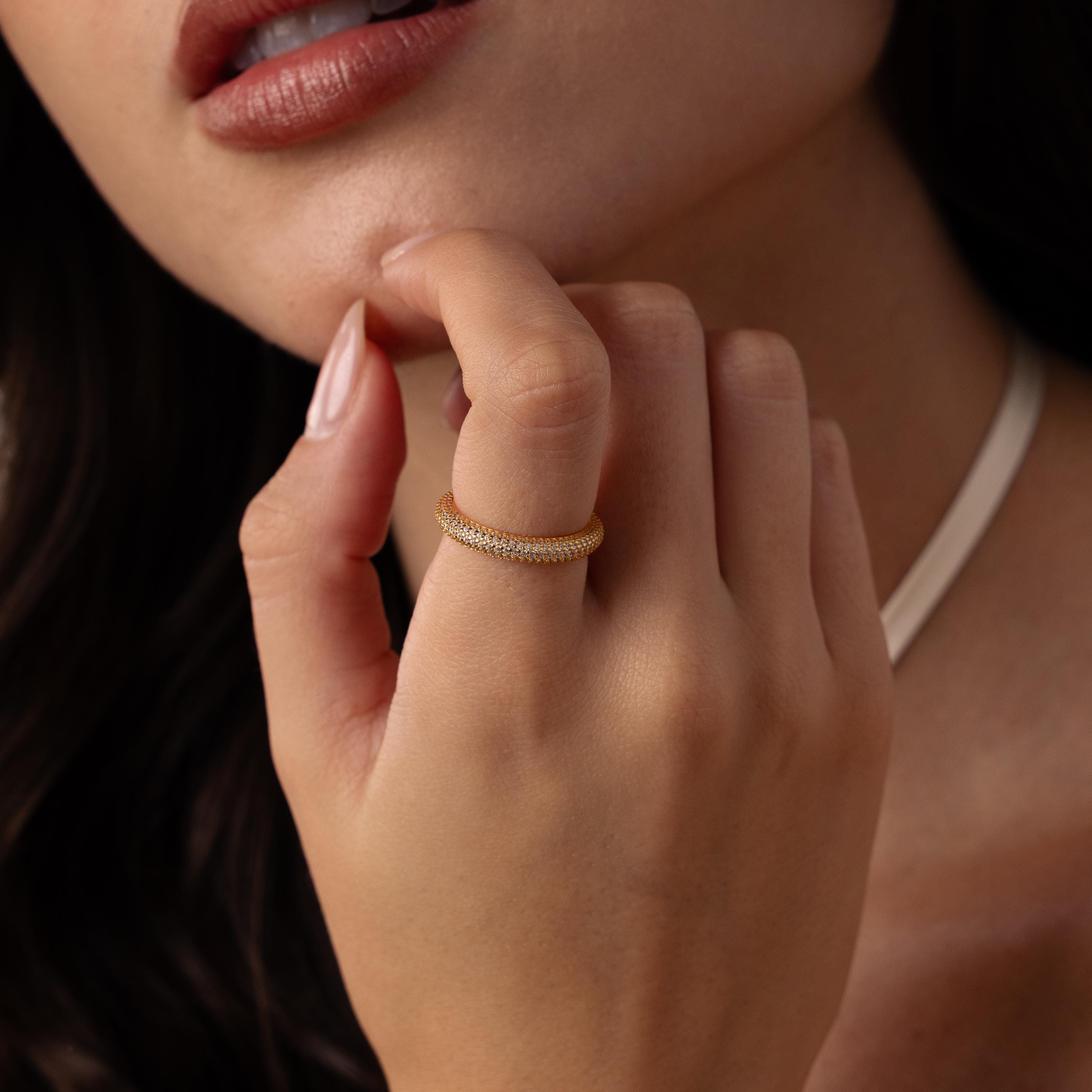 A woman wears the Skinny Pave Stacking Ring, sparkling with pave stones, on her finger as she raises her hand near her face, lips softly parted.