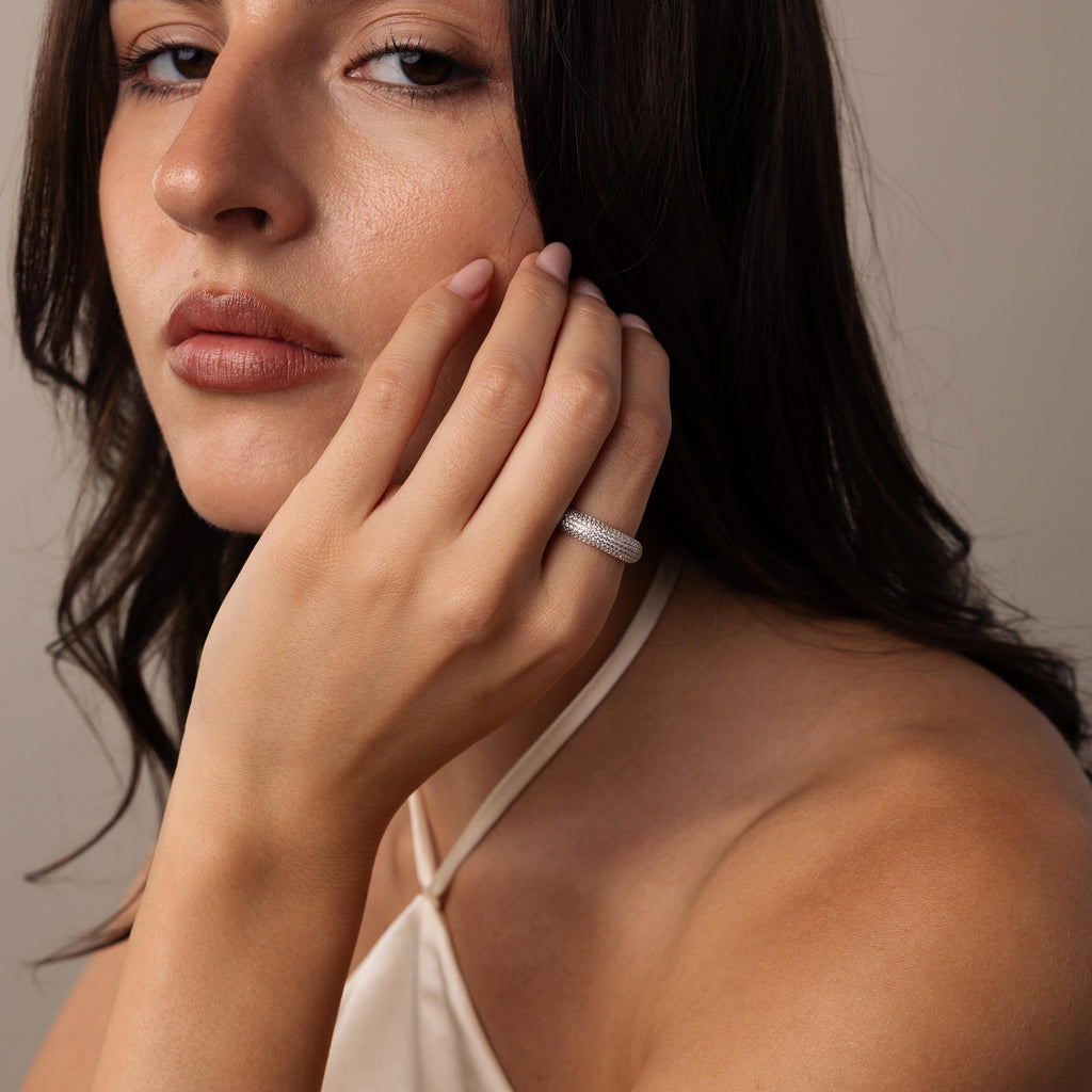 A woman with long brown hair wears a halter top and the Bold Pave Stacking Ring, resting her hand on her face.