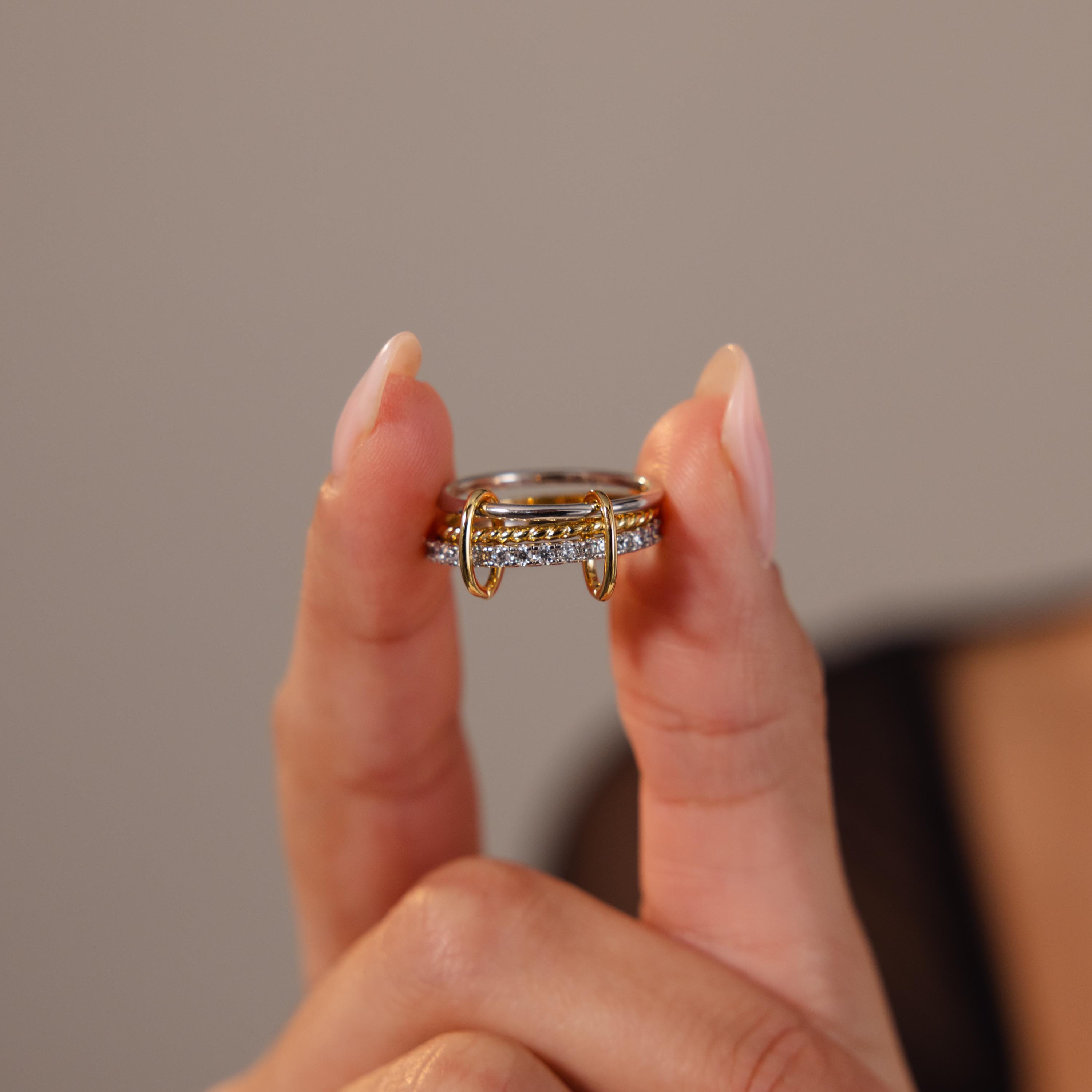 A hand with manicured nails holds the Pave Mixed Metal Linked Ring Set between two fingers, highlighting this versatile jewelry piece.