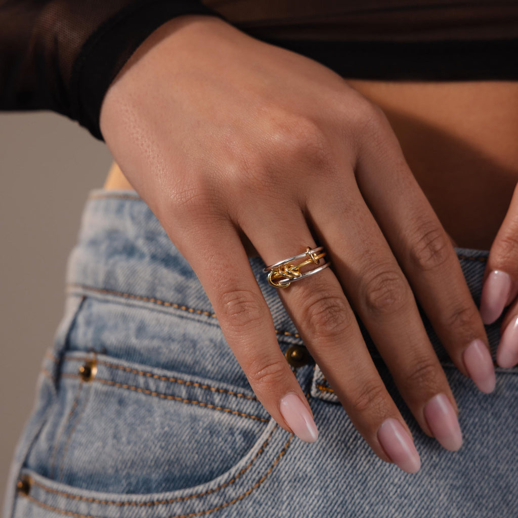 A hand with manicured nails wears the Mixed Metal Linked Ring Set, resting on the pocket of blue jeans.
