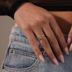 A hand with manicured nails wears the Mixed Metal Linked Ring Set, resting on the pocket of blue jeans.
