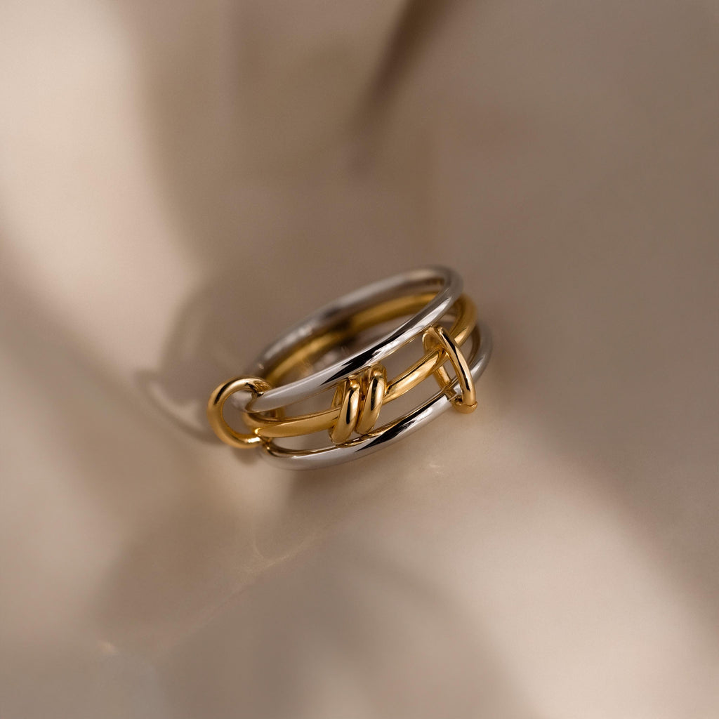 A meaningful jewelry piece, the Mixed Metal Linked Ring Set showcases gold and silver chain links, elegantly displayed on a soft beige surface.