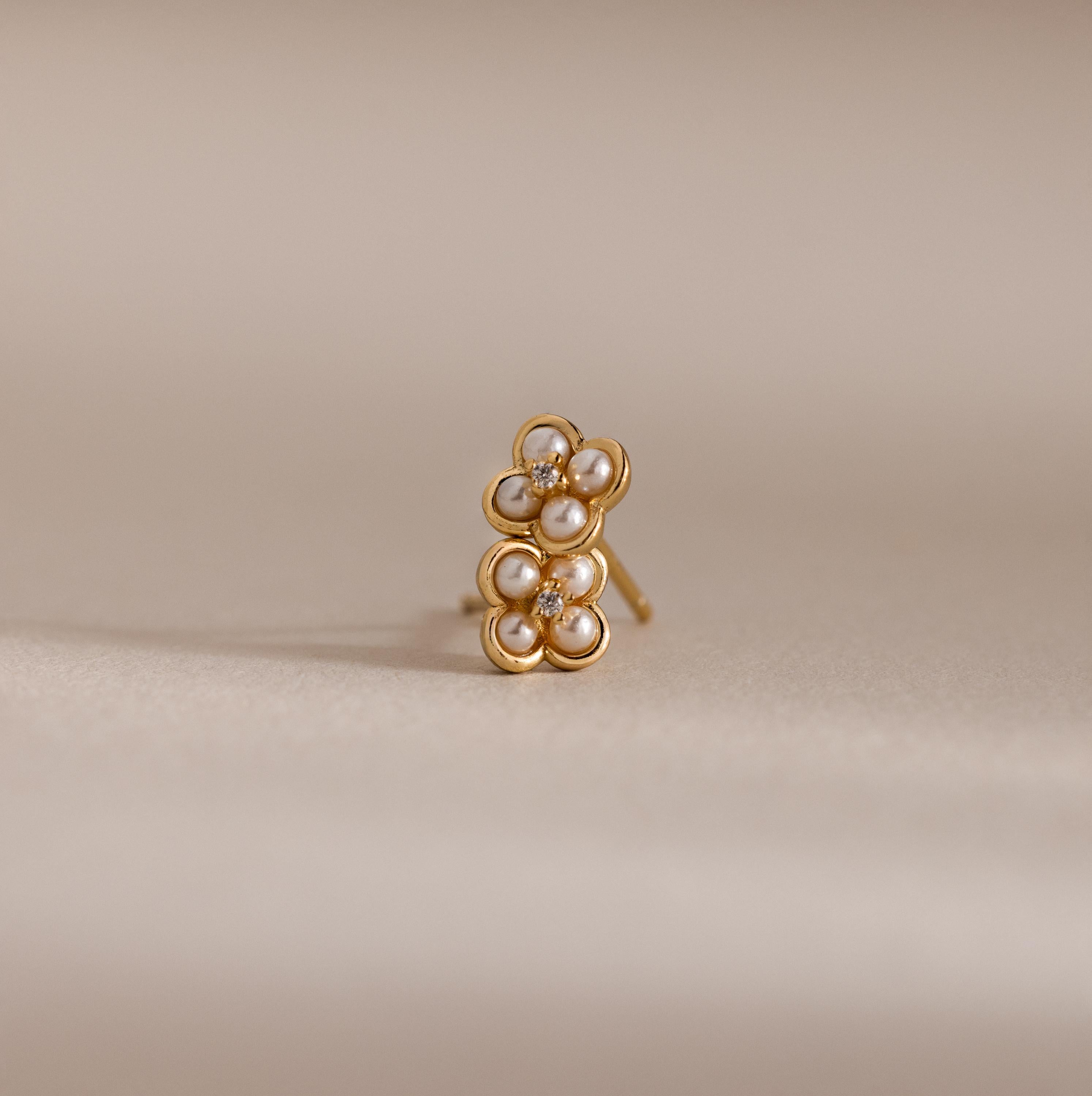 Rounded Pearl Flower Studs in 18K Gold feature pearl centers and diamond-like accents, making them perfect for bridesmaid jewelry. These elegant flower studs stand out beautifully against a neutral beige background.