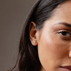 Close-up of a woman's ear wearing Rounded Pearl Flower Studs in 18K Gold, featuring an elegant flower design—ideal as bridesmaid jewelry—with part of her face visible.