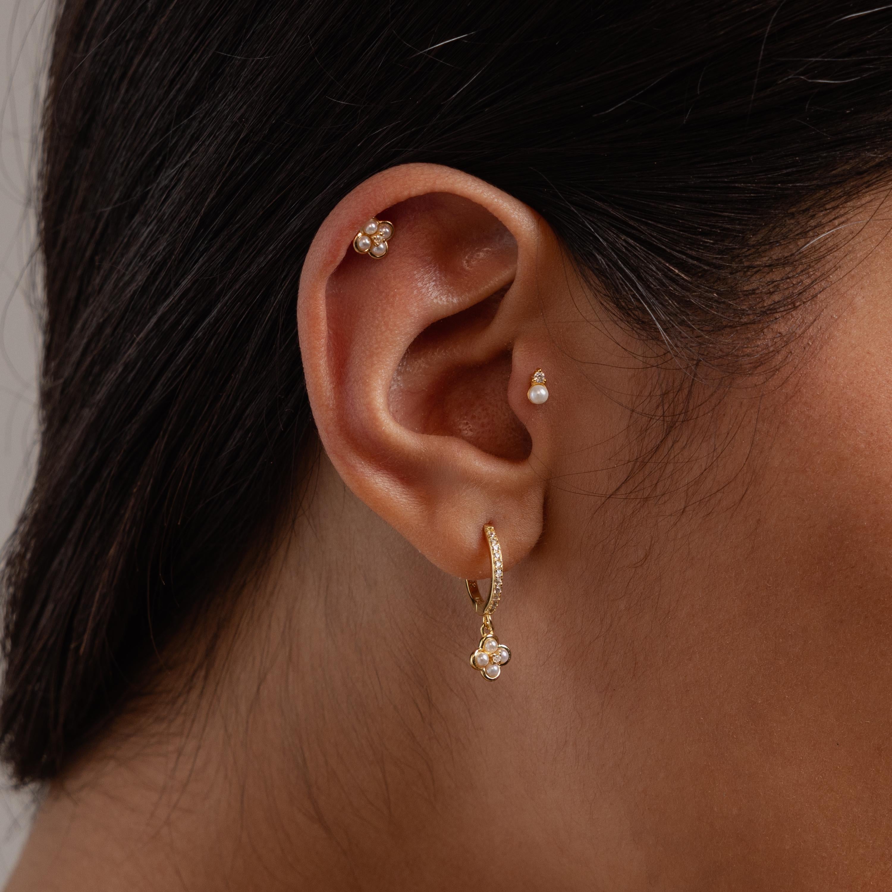 Close-up of an ear adorned with Rounded Pearl Flower Studs in 18K Gold and other elegant earrings—ideal for bridesmaid jewelry.