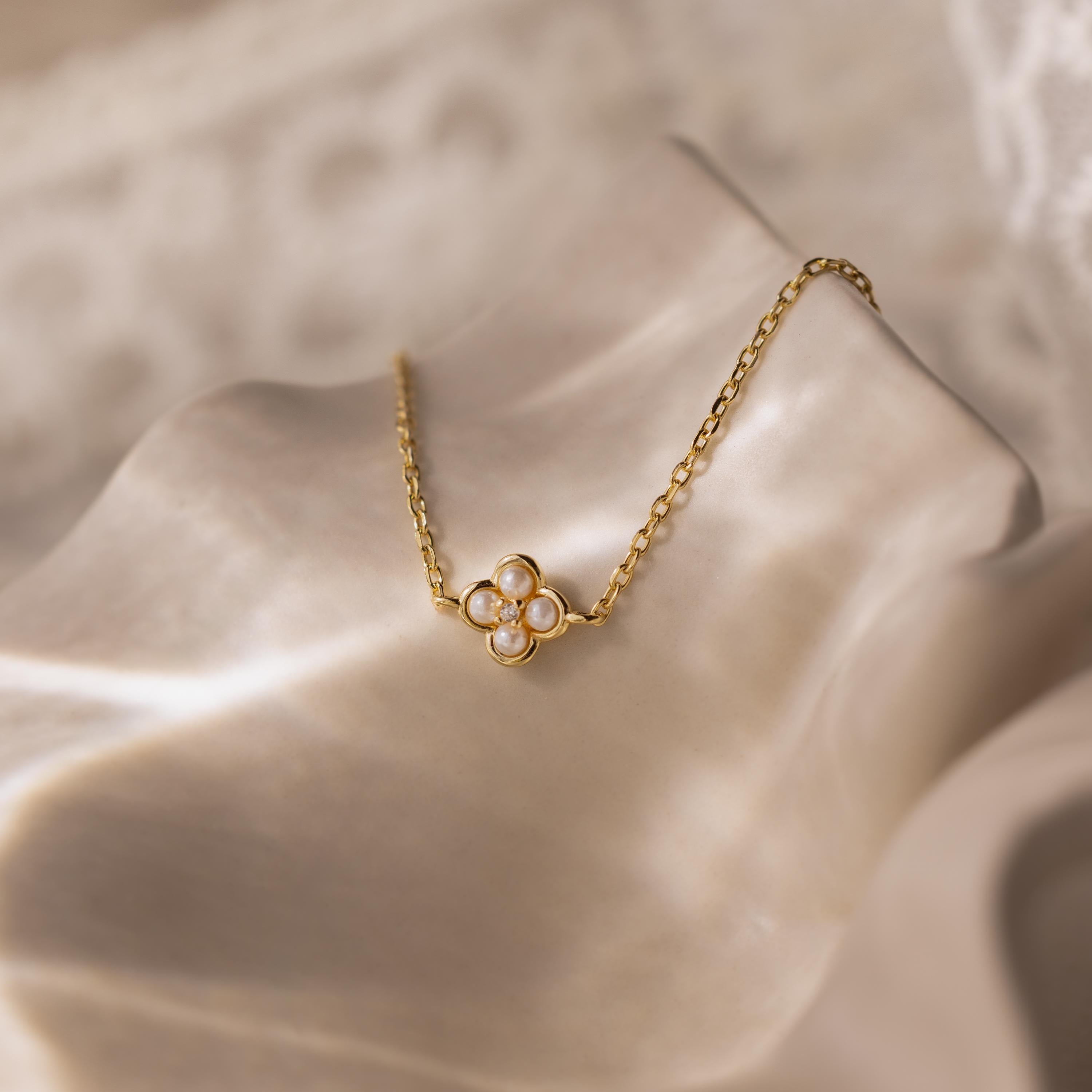 The Rounded Pearl Flower Bracelet in 18K Gold, adorned with four small pearls, is displayed on soft, wavy cream fabric—a beautiful piece for fans of delicate jewelry.