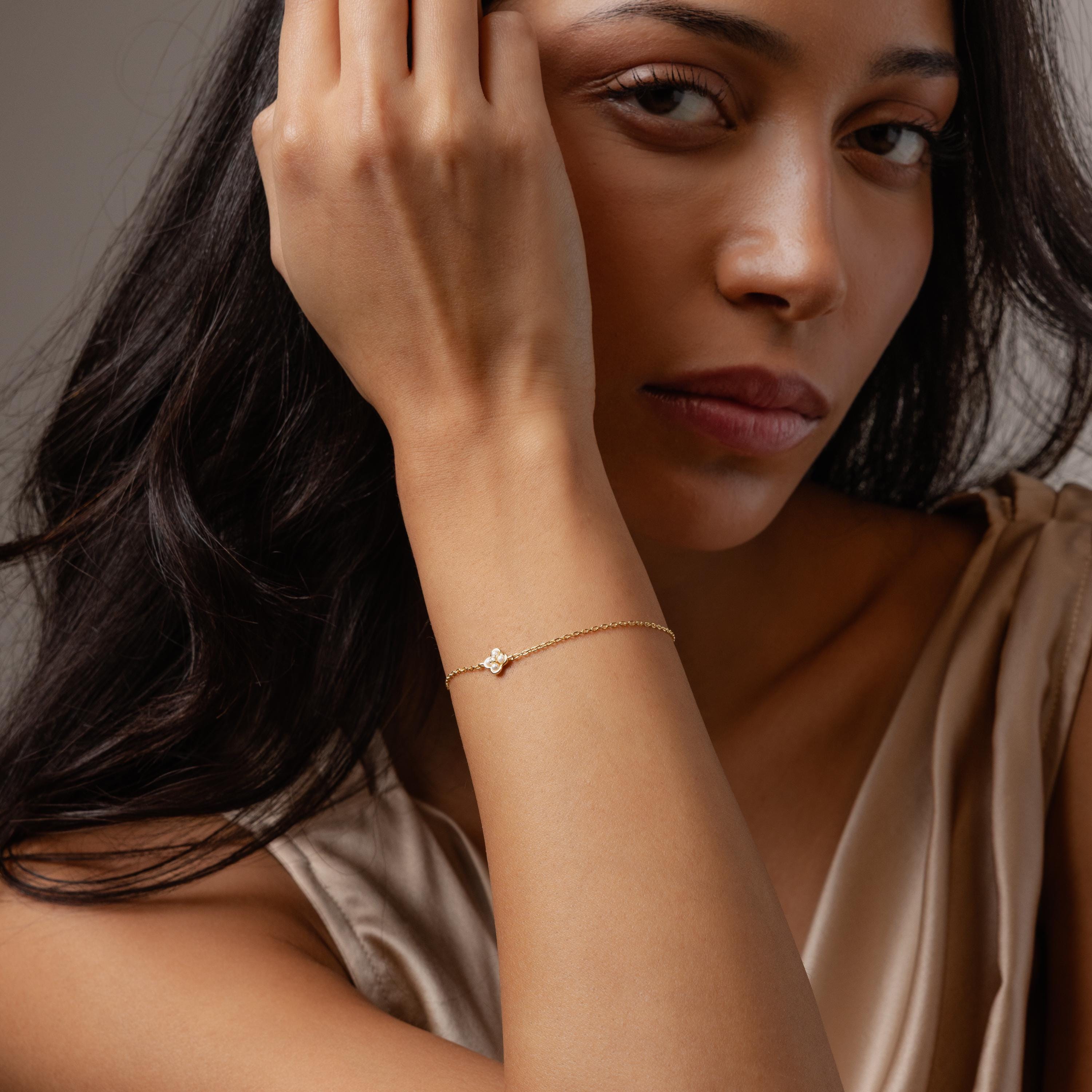 Woman in beige top wearing the Rounded Pearl Flower Bracelet in 18K Gold, featuring a delicate floral design with pearls, resting her hand on her face.