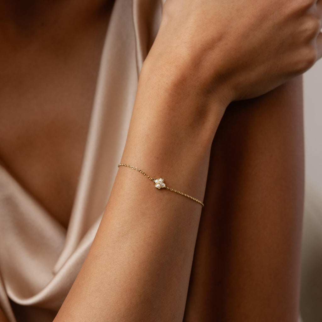 A woman wearing the Rounded Pearl Flower Bracelet, featuring a delicate gold chain with a floral pearl charm, and dressed in a silky beige top.