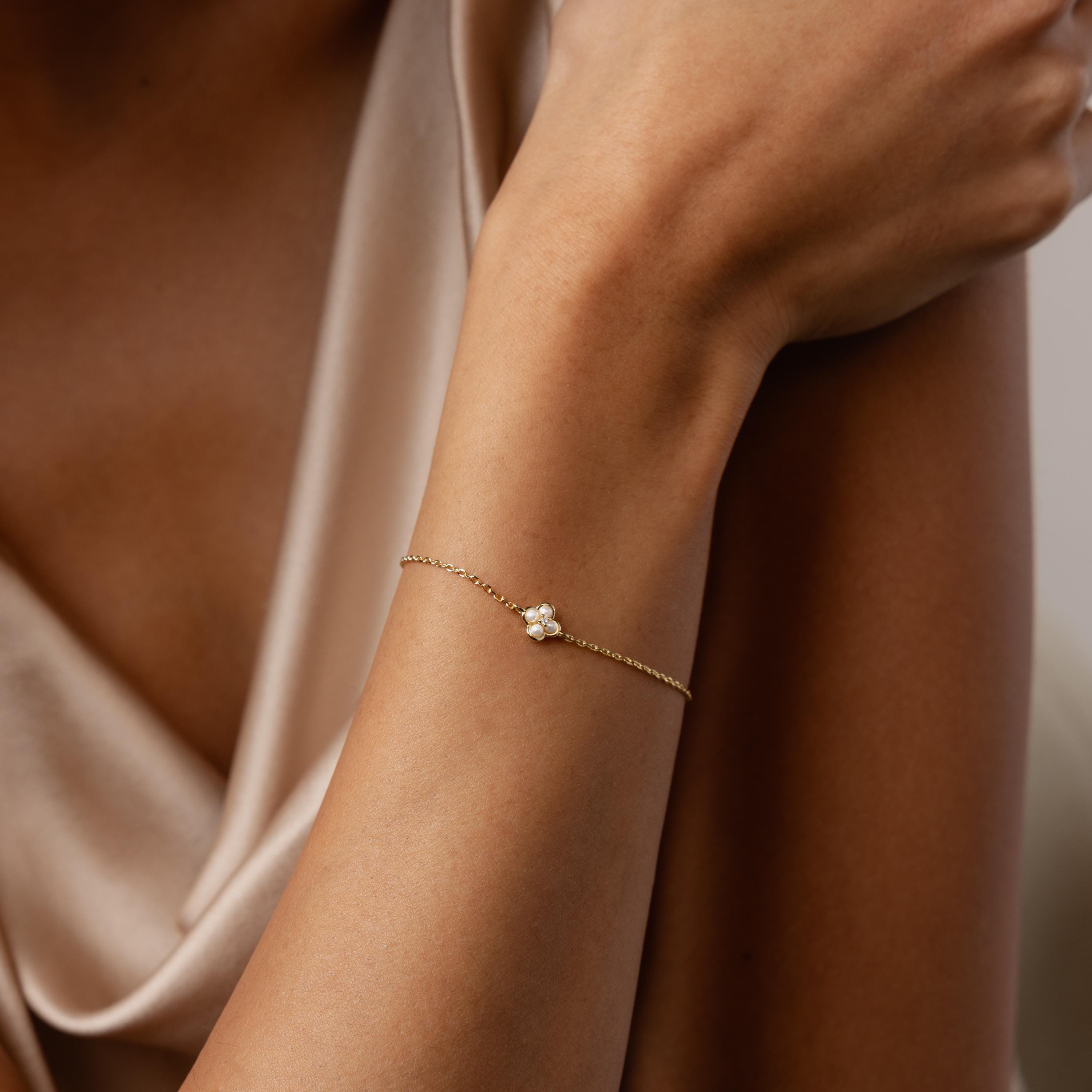 A woman wearing the Rounded Pearl Flower Bracelet, featuring a delicate gold chain with a floral pearl charm, and dressed in a silky beige top.