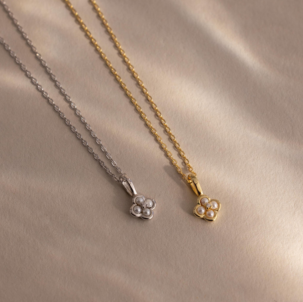Two elegant Rounded Pearl Flower Necklaces—one in silver and one in gold—each feature a delicate pearl flower pendant, gracefully presented on a beige background.
