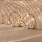 The Statement Pearl Hoops in 18K Gold showcase quiet luxury with gleaming gold hoops and luminous white pearls set against a textured beige backdrop.