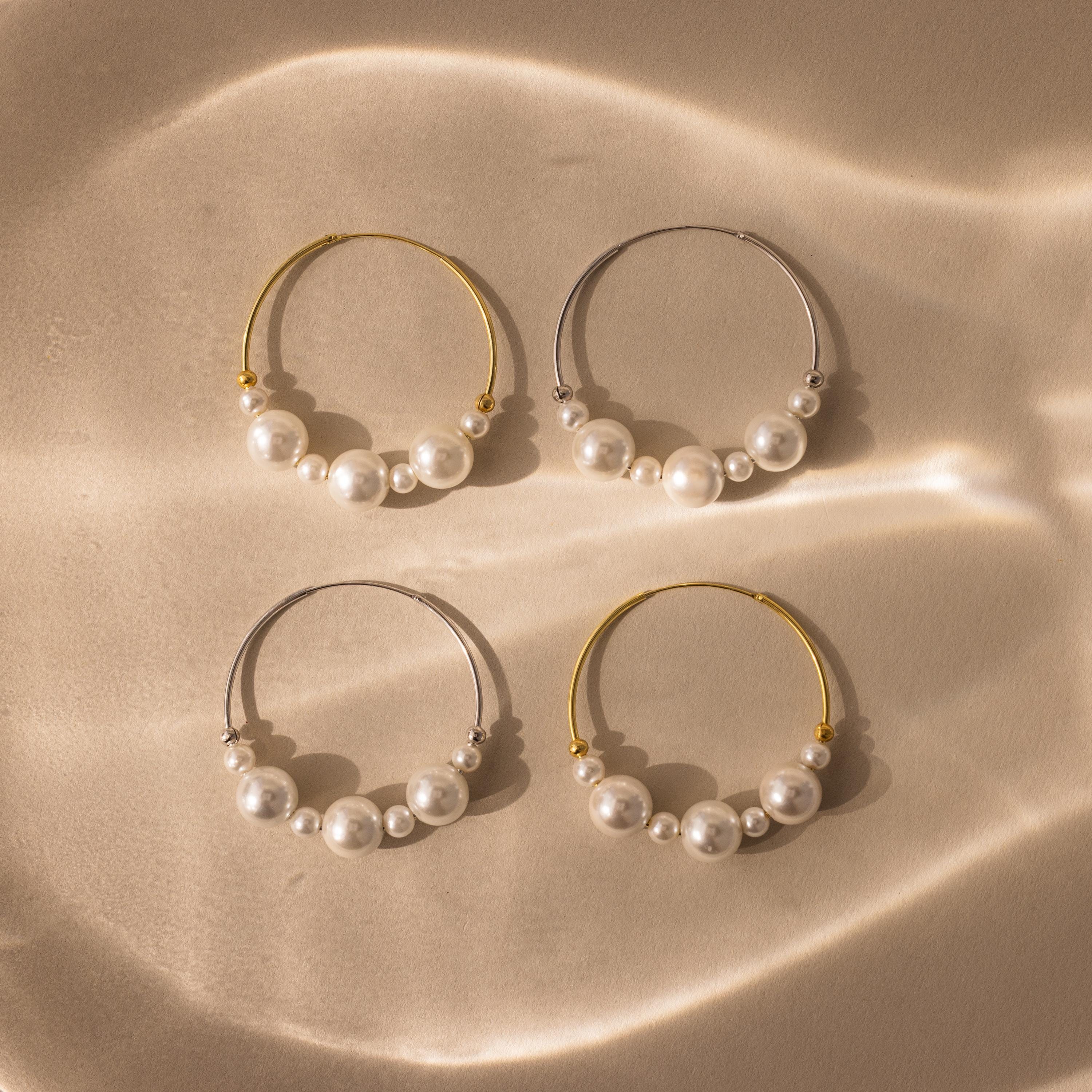 Statement Pearl Hoops featuring an open hoop design—two accented with gold, two with silver—are displayed on a beige textured surface.