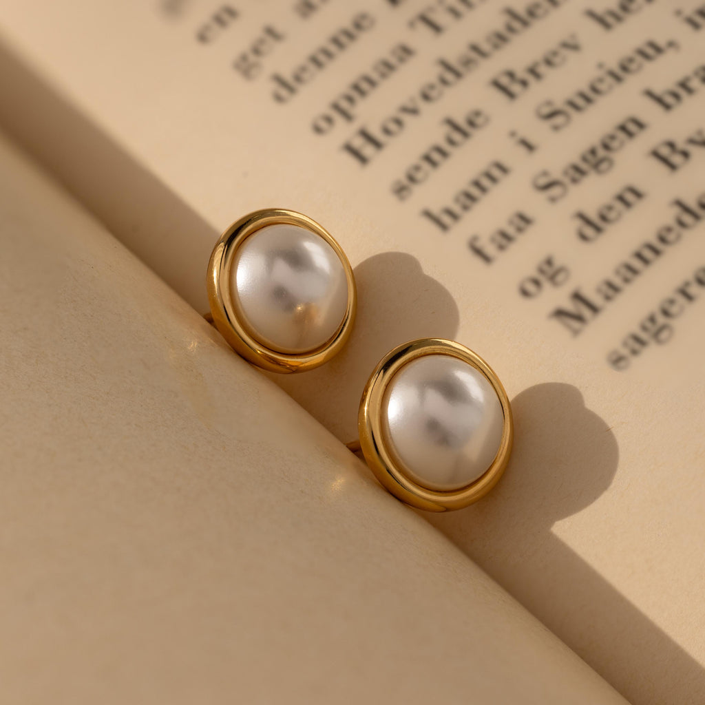 Pearl Bezel Studs rest elegantly on the pages of an open book, capturing the timeless charm of classic jewelry.