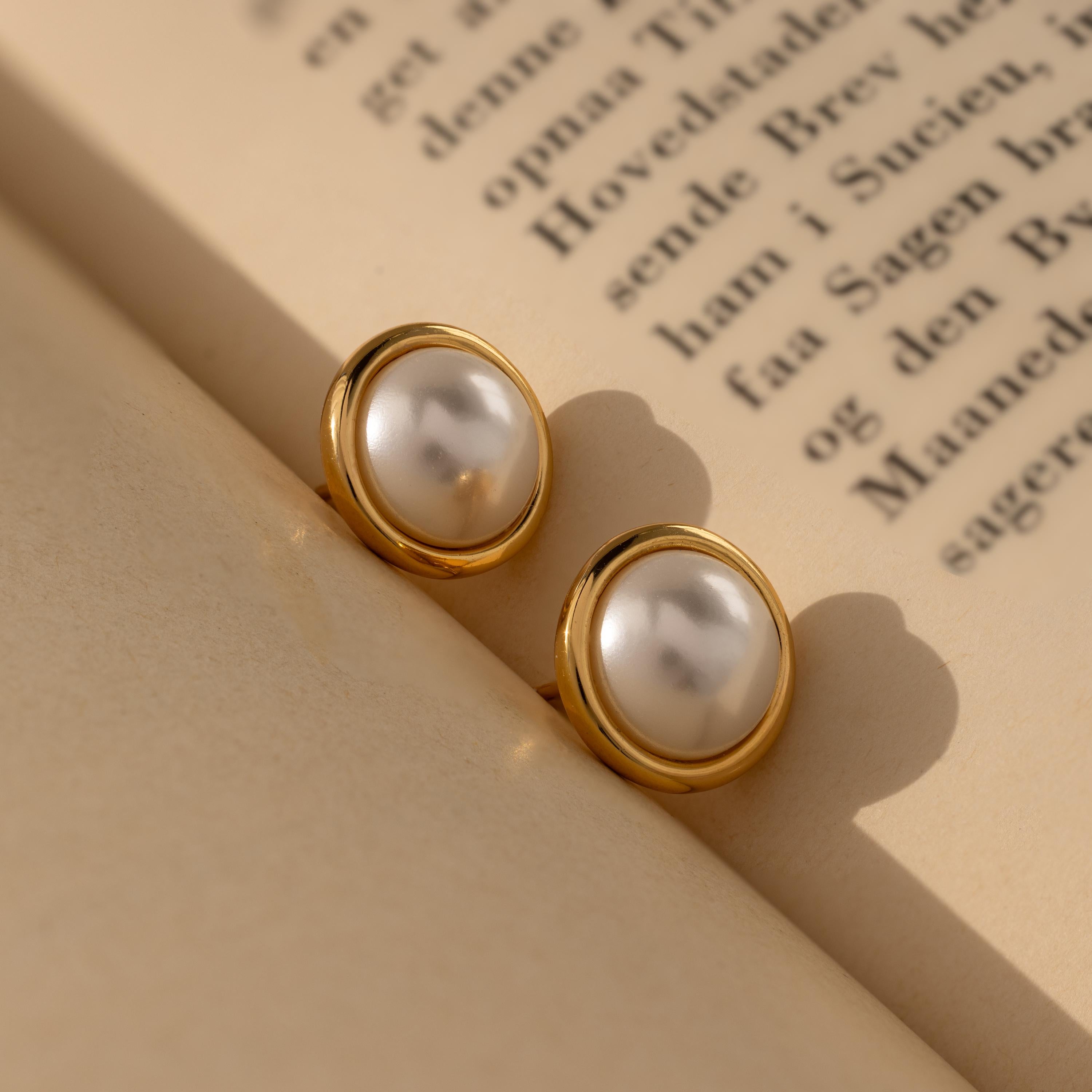 Pearl Bezel Studs rest elegantly on the pages of an open book, capturing the timeless charm of classic jewelry.