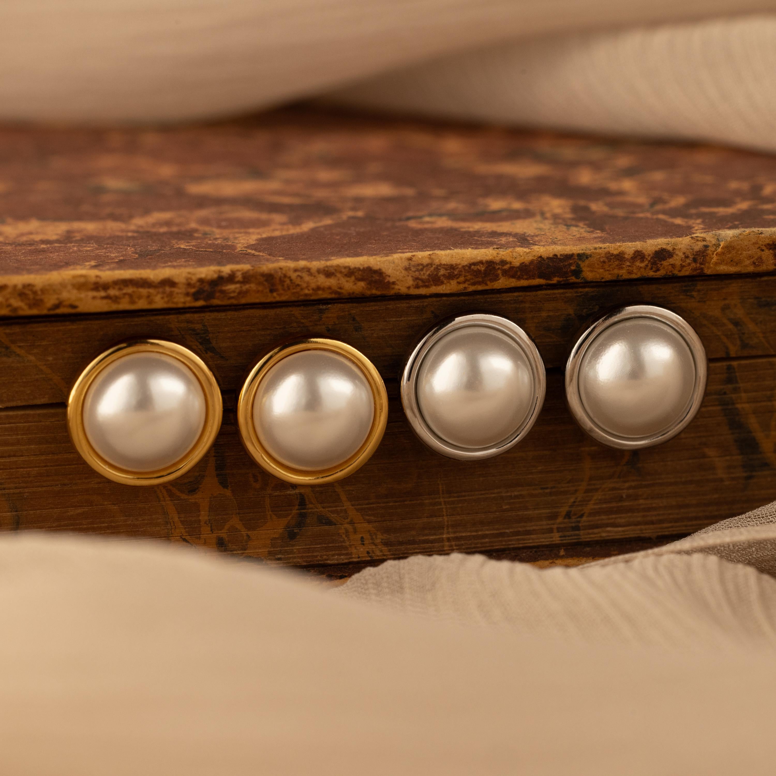 The Pearl Bezel Studs, available in both gold and silver bezels, are displayed on a rustic surface—a timeless addition to your classic jewelry collection.